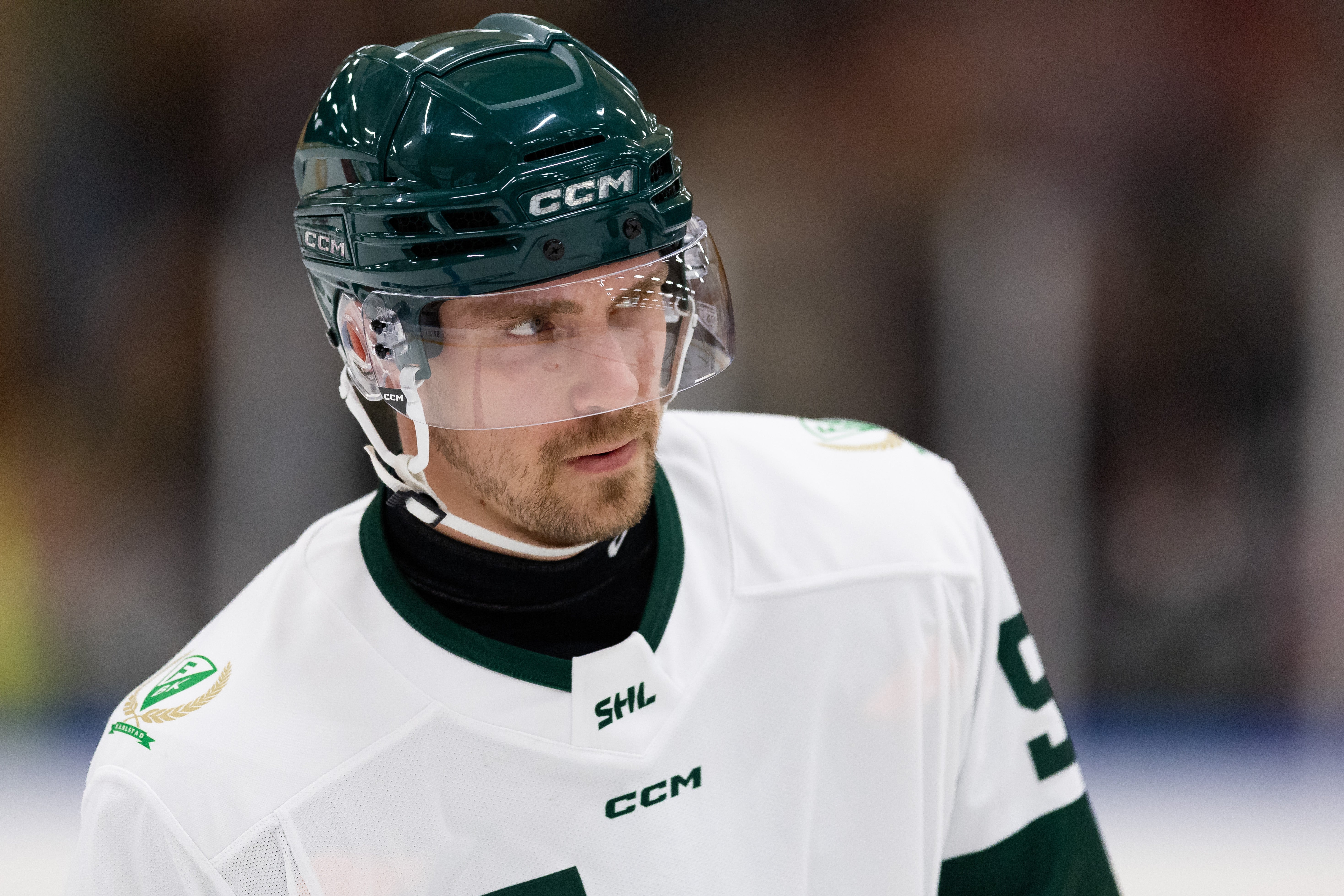 Ishockeyspelare i vit och grön matchdräkt med CCM-hjälm under en ishockeymatch.
