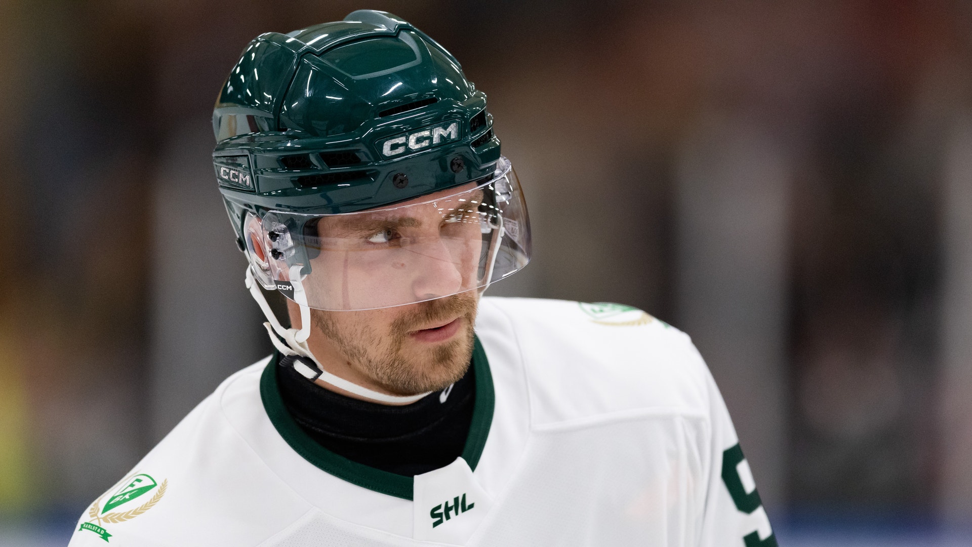 Ishockeyspelare i vit och grön matchdräkt med CCM-hjälm under en ishockeymatch.