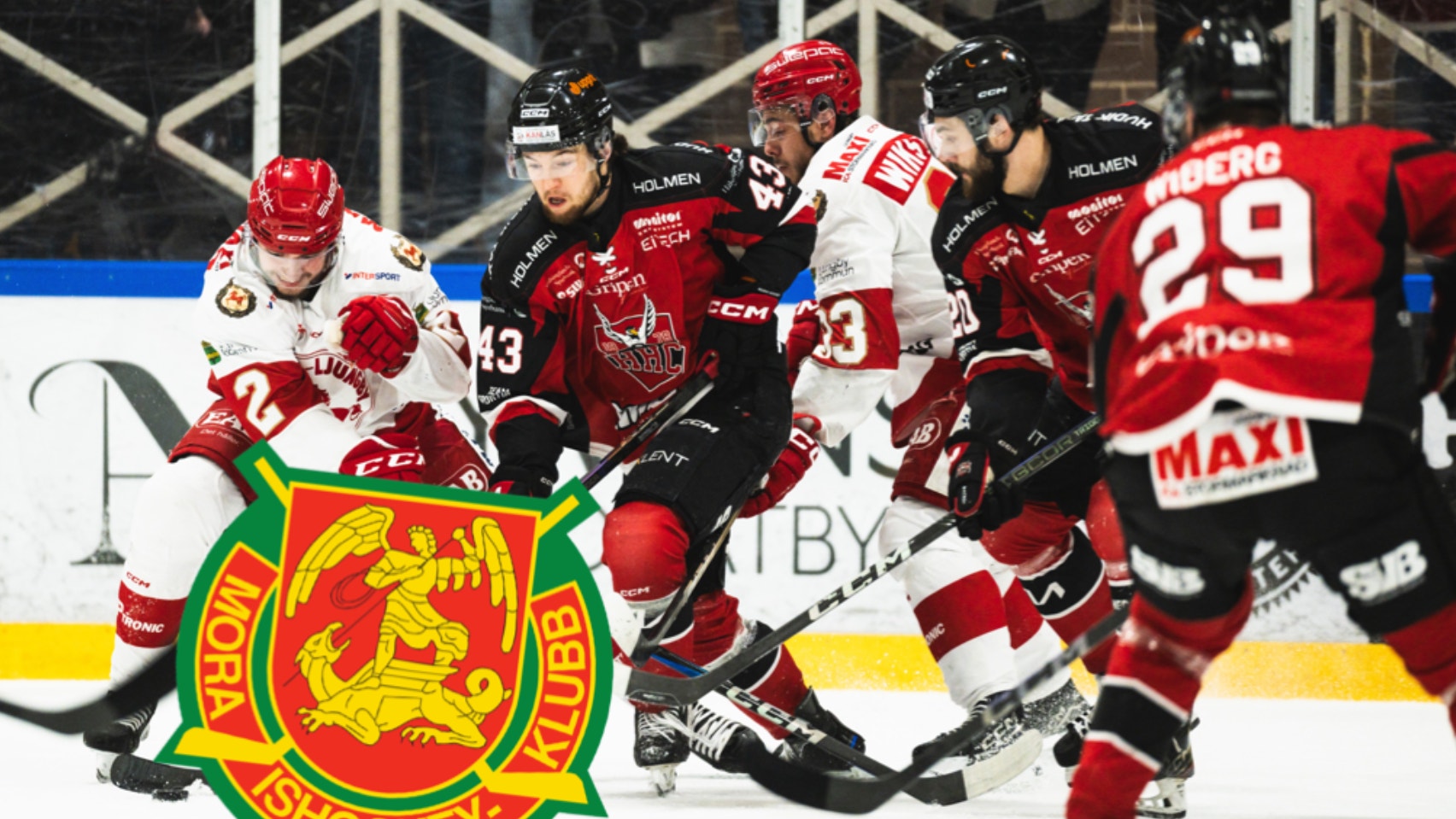 Hockeymatch mellan två lag där spelare i röda och vita tröjor spelar mot spelare i svarta tröjor. Rögle Hockeys logga syns i förgrunden.
