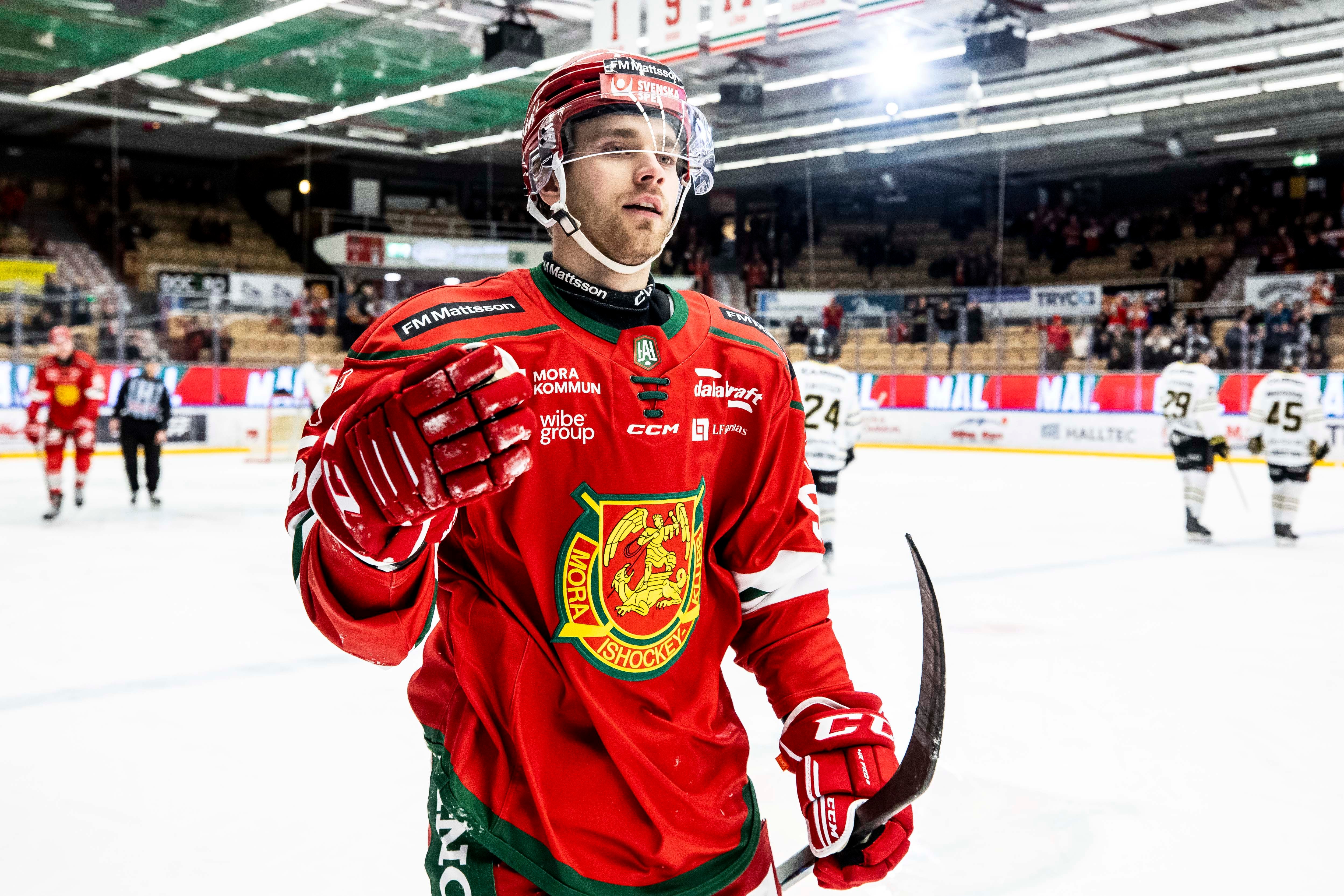 Ishockeyspelare i röd landslagströja viftar till publiken under en match i en ishall.