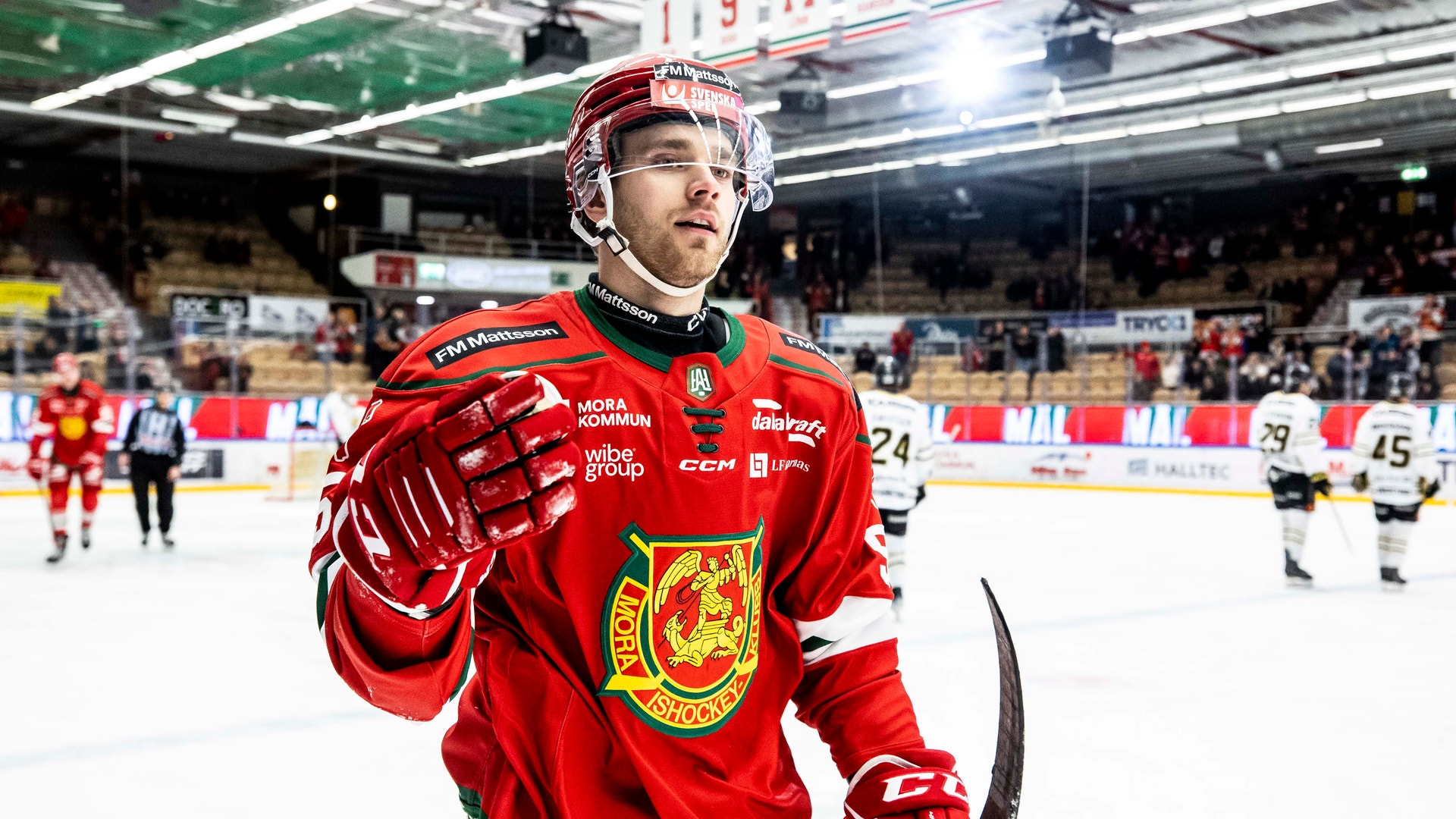 Ishockeyspelare i röd landslagströja viftar till publiken under en match i en ishall.