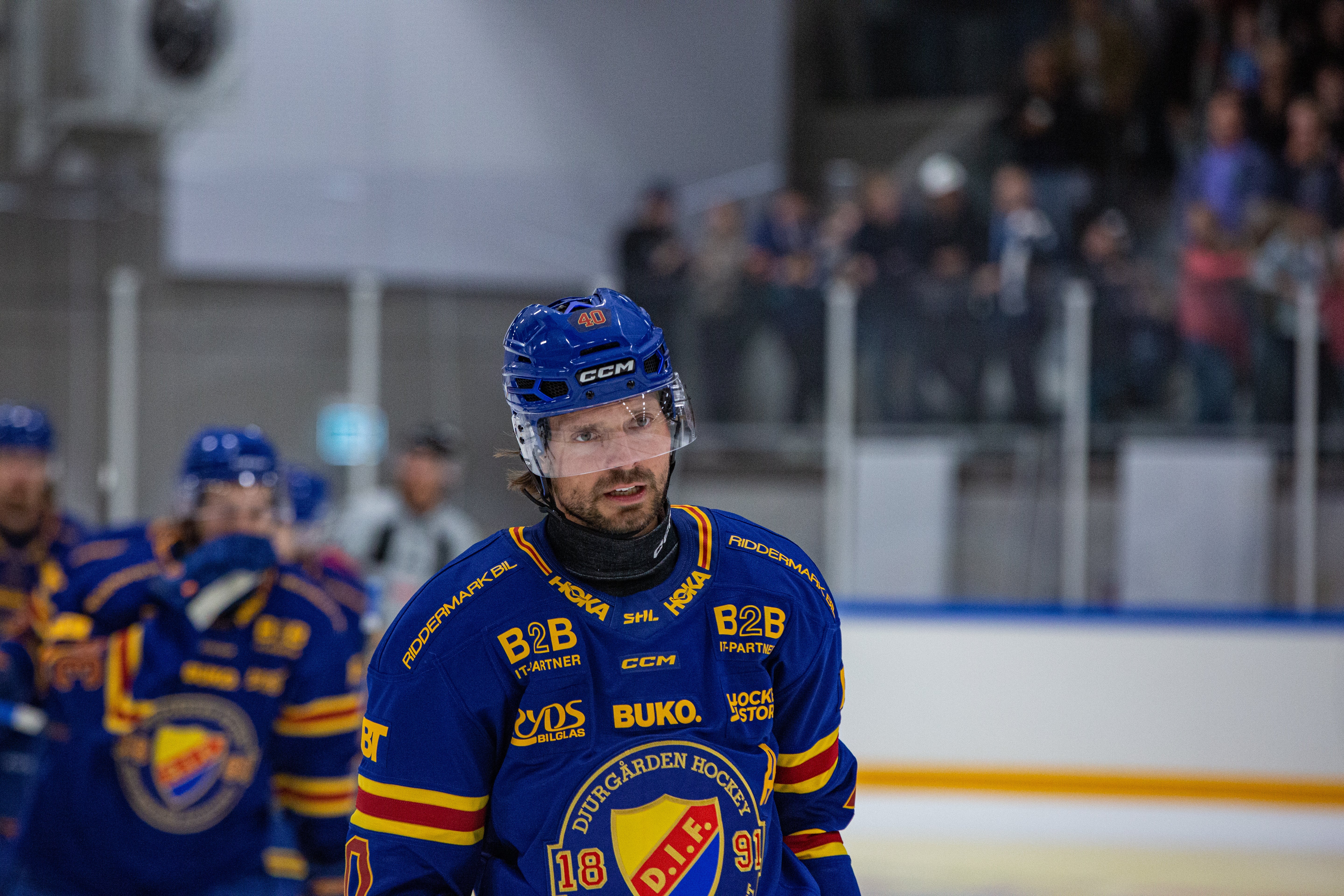 Ishockeyspelare i blå och gul tröja står på isen under en match med publik i bakgrunden.