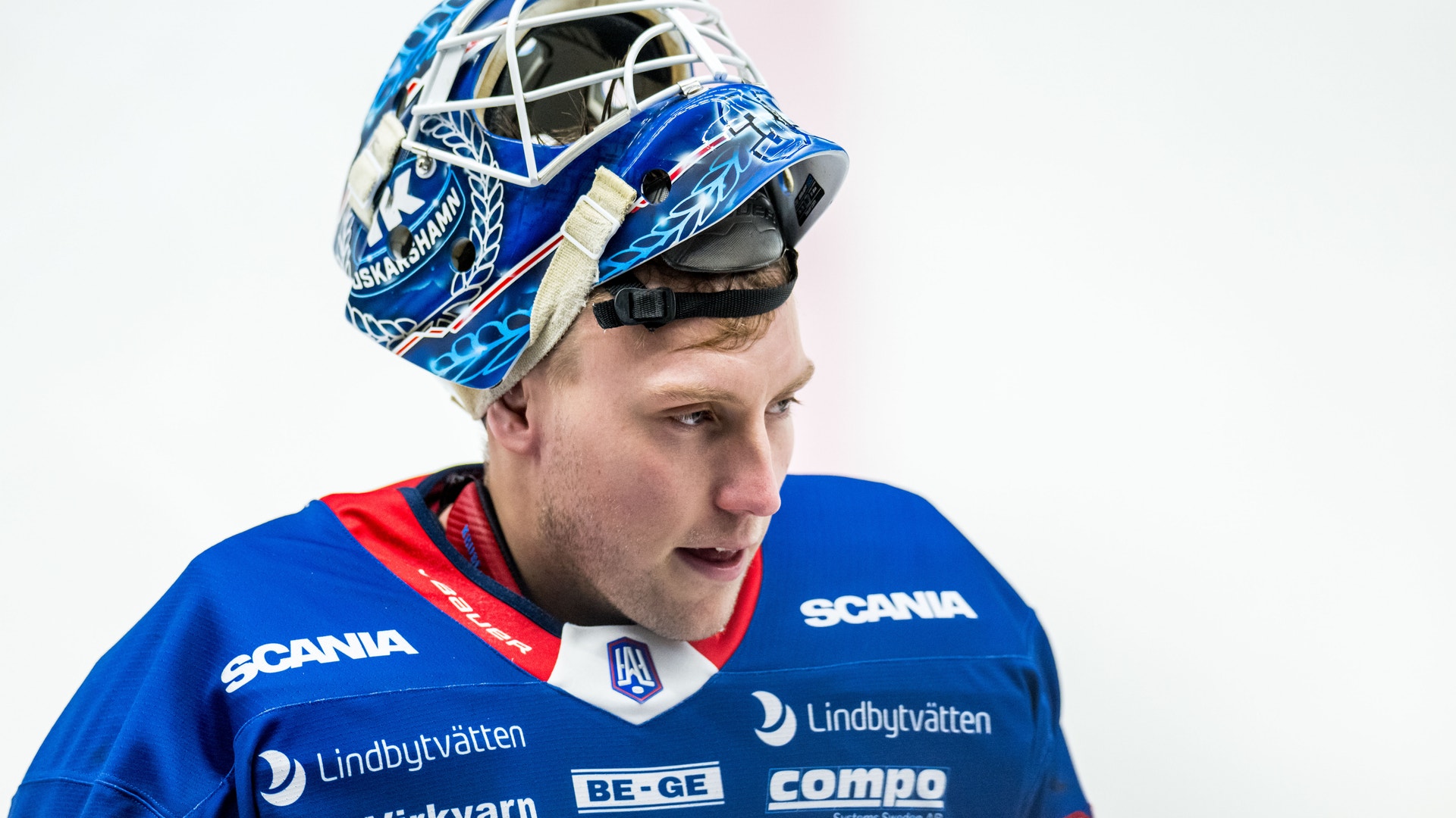 Ishockeyspelare i blå uniform och målvaktsmask med blå och vita mönster.