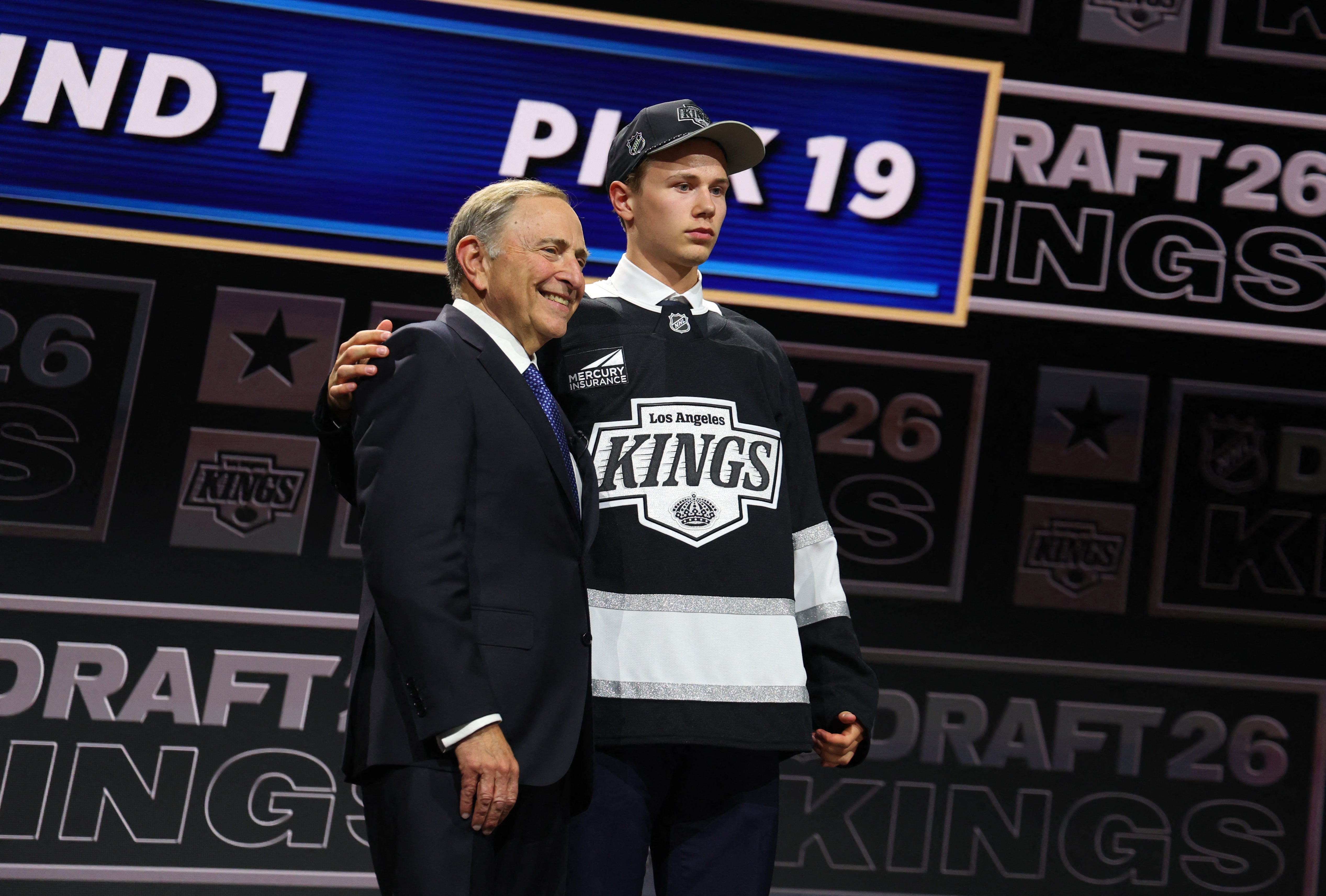 En ung hockeyspelare i Los Angeles Kings-tröja presenteras på scenen tillsammans med en äldre man i kostym under ett NHL-draft-event.