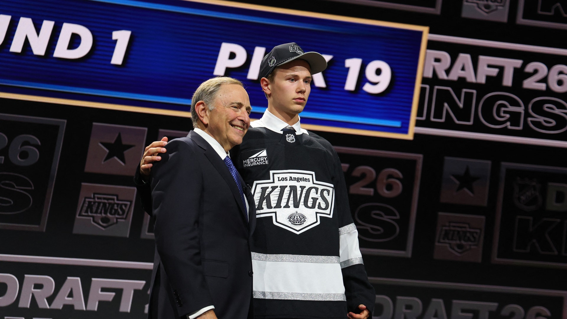 En ung hockeyspelare i Los Angeles Kings-tröja presenteras på scenen tillsammans med en äldre man i kostym under ett NHL-draft-event.