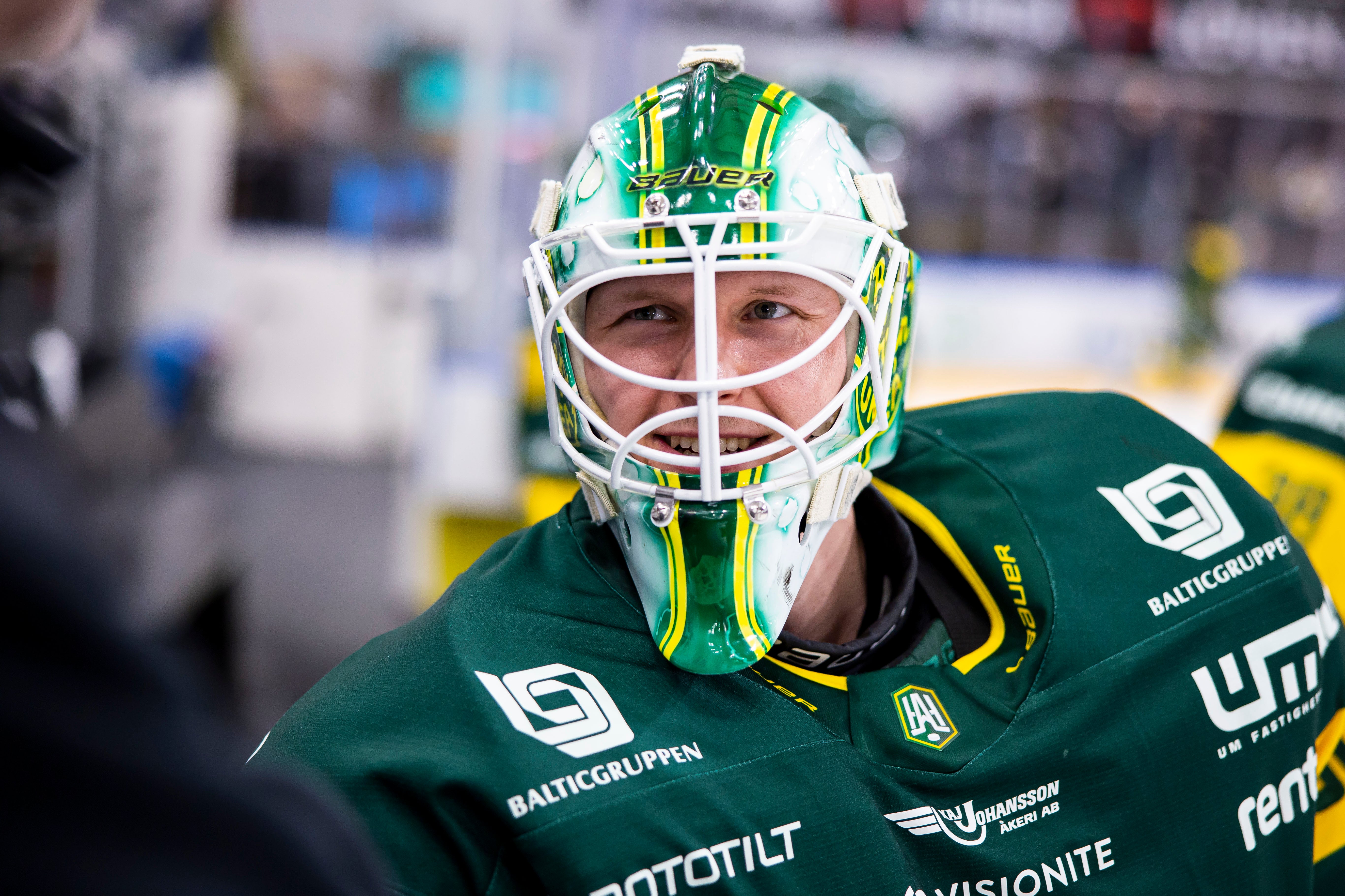 Porträtt av en ishockeyspelare i målvaktsutrustning med grön och gul dräkt och målvaktsmask.