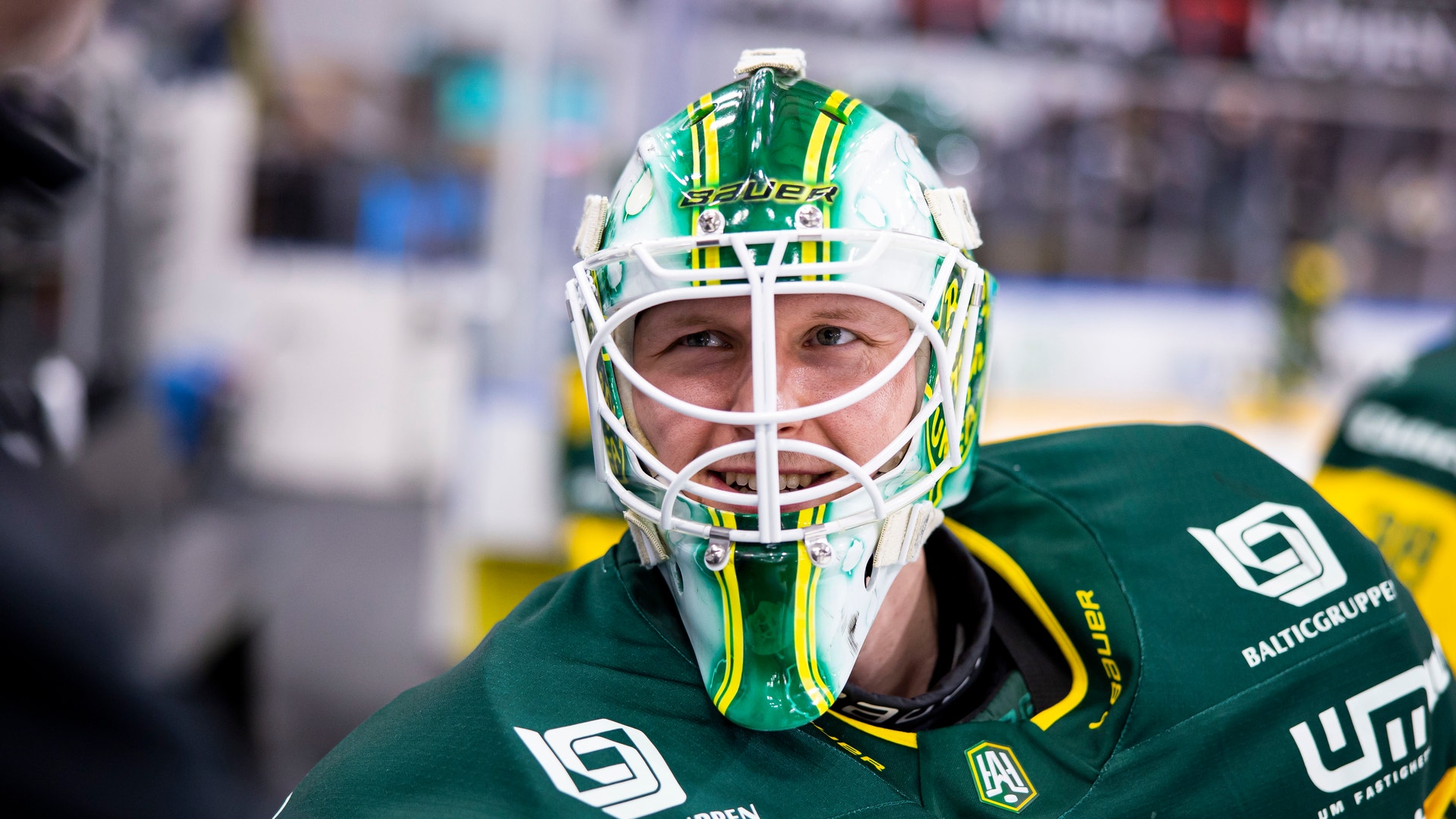 Porträtt av en ishockeyspelare i målvaktsutrustning med grön och gul dräkt och målvaktsmask.