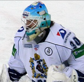 Ishockeyspelare i vit utrustning med blå hjälm fotograferad framifrån på isen.