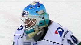 Ishockeyspelare i vit utrustning med blå hjälm fotograferad framifrån på isen.