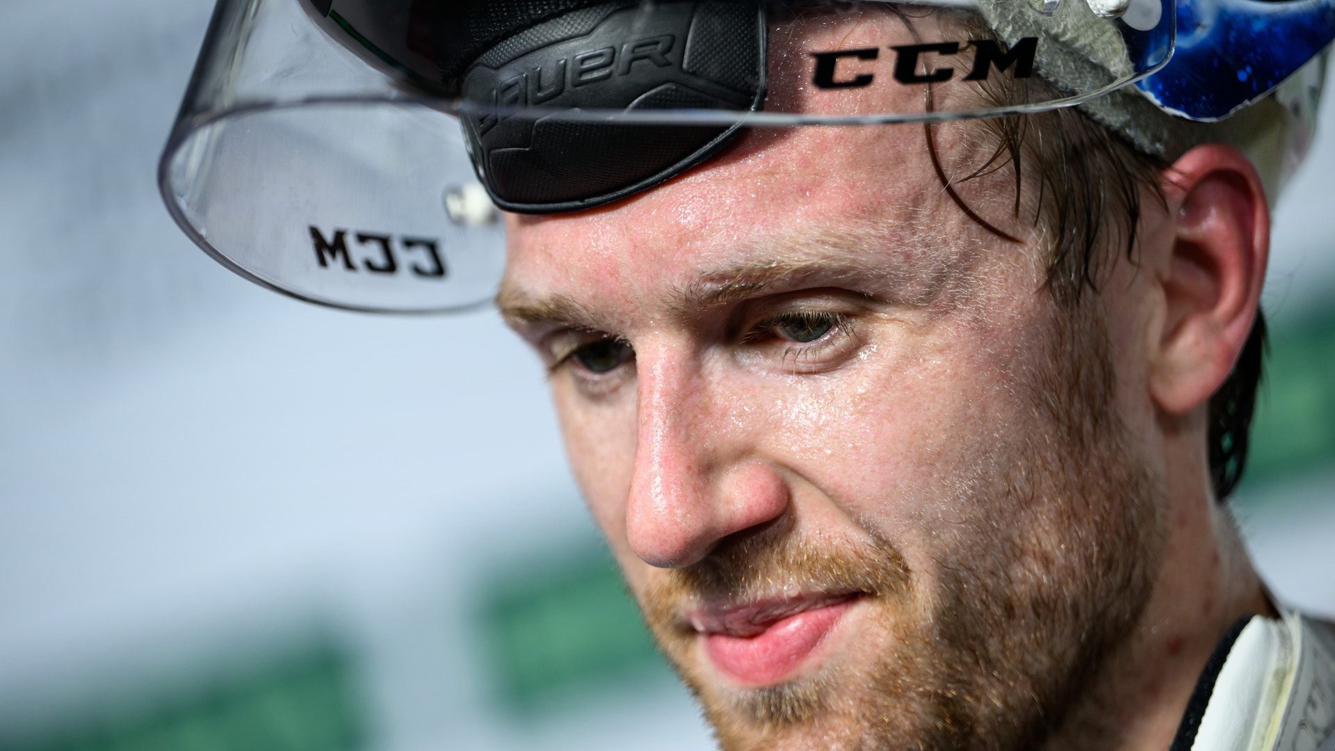 Ishockeyspelare firar på isen med upphöjd arm och hockeyklubbe. Spelaren bär svart och vit tröja med röda detaljer. Publik syns på läktaren i bakgrunden.