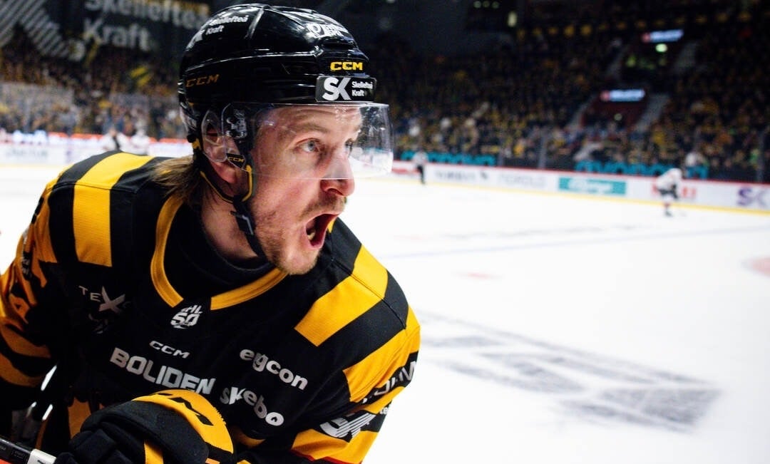 En ishockeyspelare i gul och svart matchtröja skriker ut ett känslosamt jubel på isen.