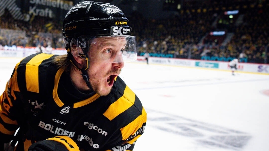 En ishockeyspelare i gul och svart matchtröja skriker ut ett känslosamt jubel på isen.
