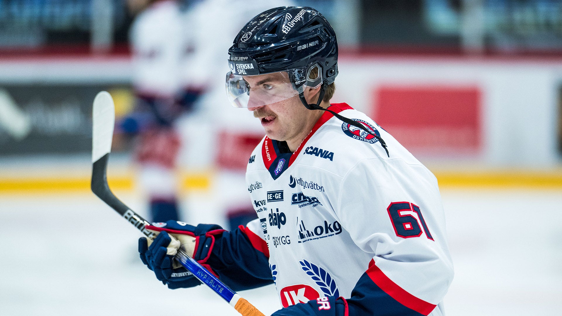 Ishockeyspelare i vit och röd tröja med nummer 6 spelar på isen. Spelaren håller en hockeyklubb och är i rörelse under en match.
