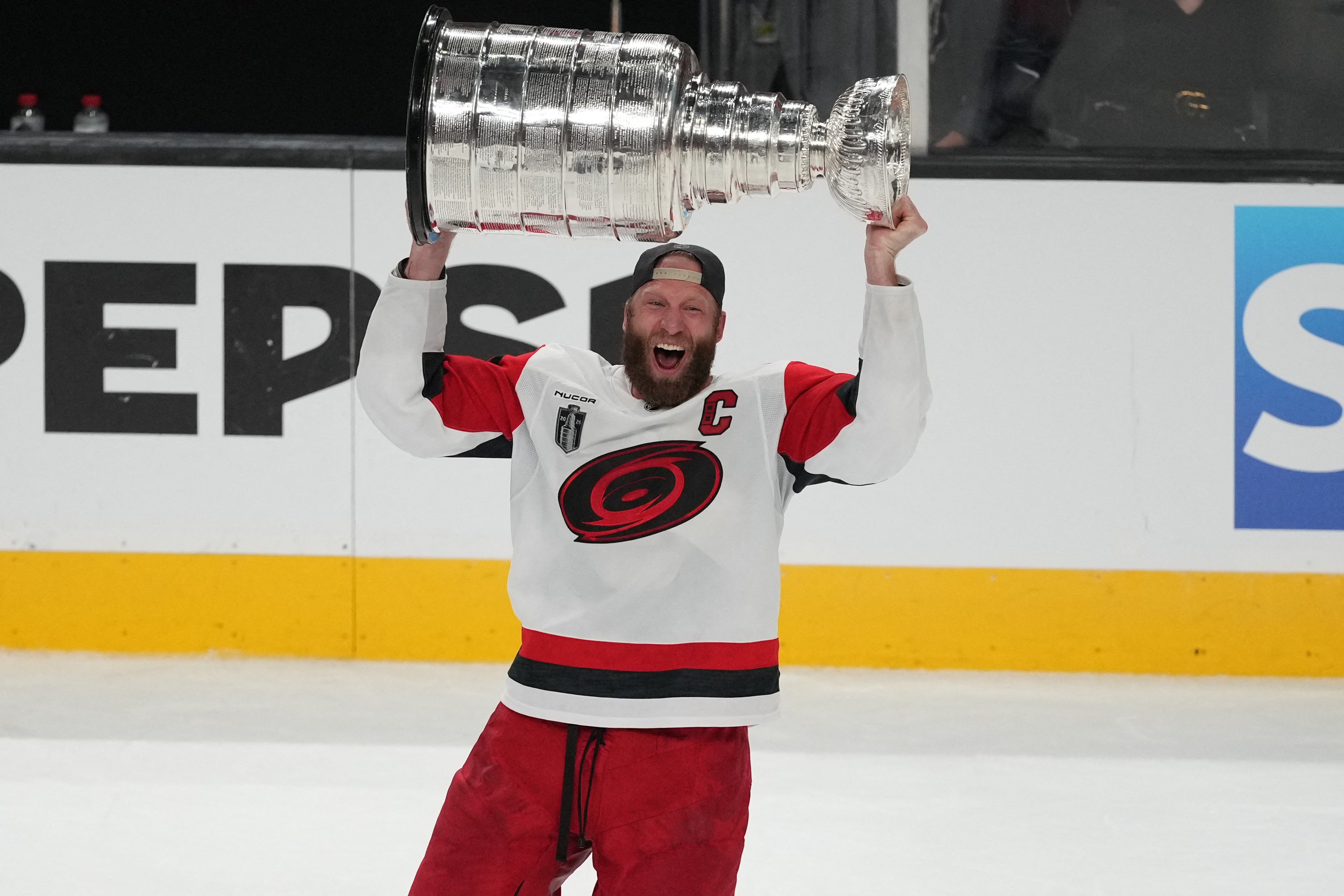 Hockeyspelar i röd och vit tröja håller Stanley Cup över huvudet på isen efter en seger.