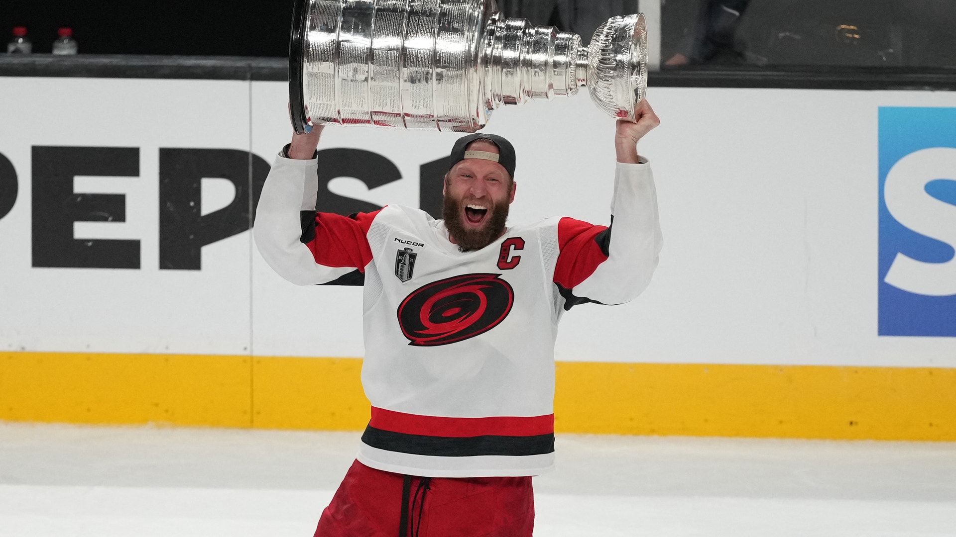 Hockeyspelar i röd och vit tröja håller Stanley Cup över huvudet på isen efter en seger.