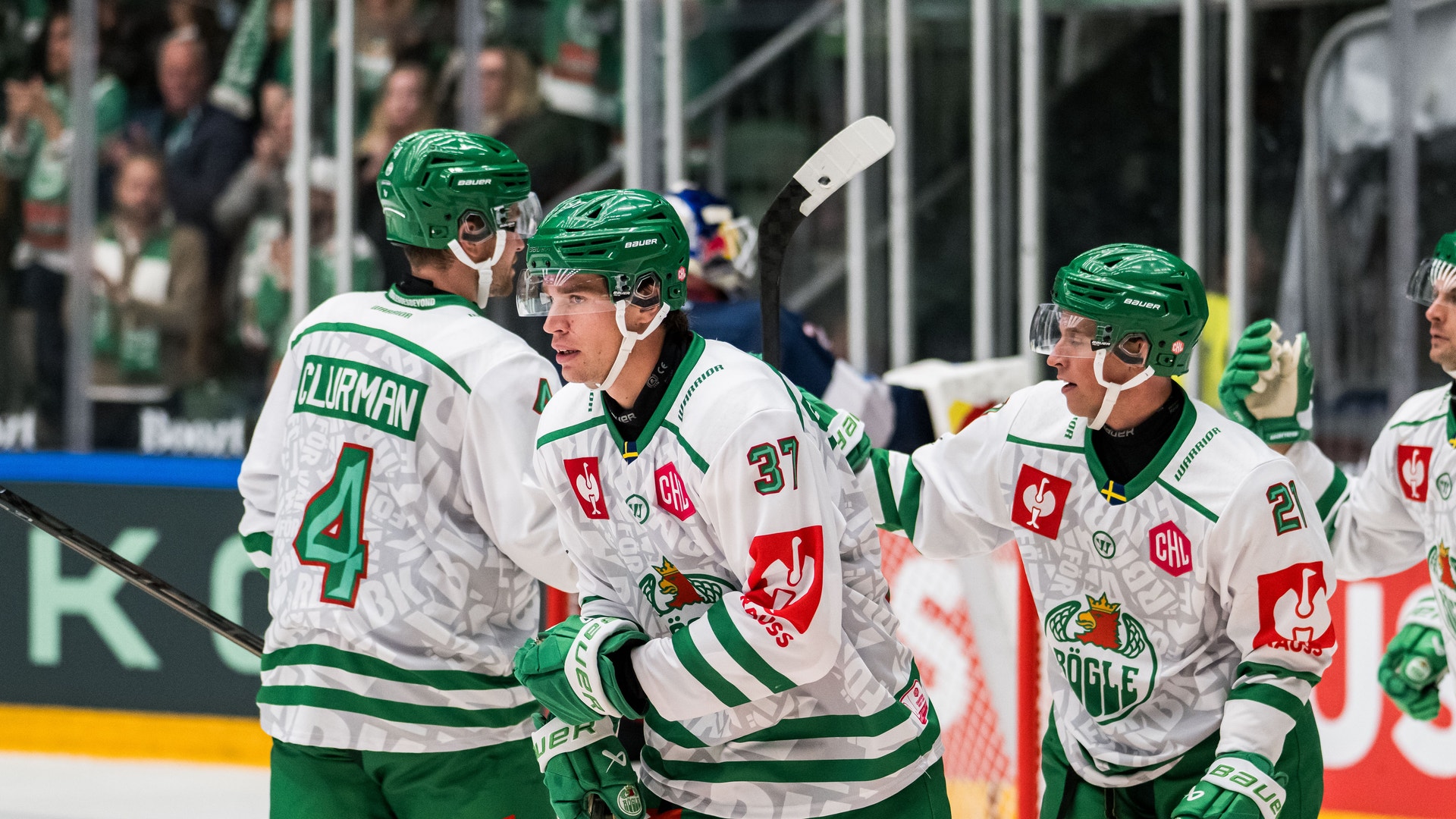 Ishockeyspelare i vita och gröna matchtröjor firar tillsammans på isen.