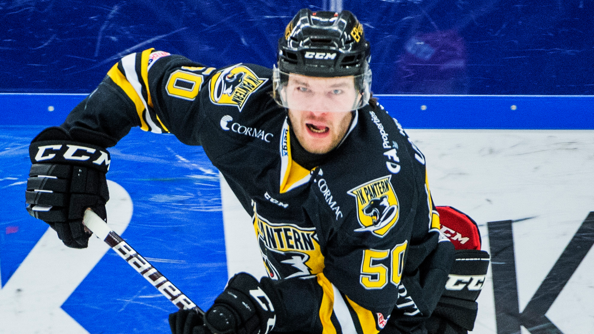 Ishockeyspelare i svart och gul matchtröja med hjälm, som åker på isen med klubban i handen.