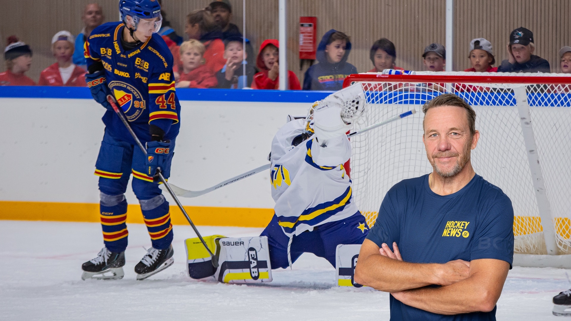 Man i mörkblå Hockey News-tröja står framför en ishockeyrink med spelare och publik i bakgrunden.
