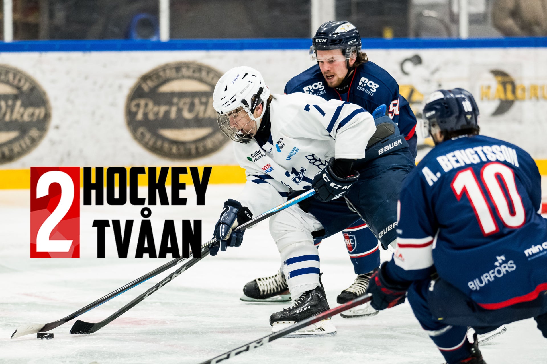 Ishockeyspelare i matchsituation, en spelare i vit matchtröja kontrollerar pucken medan motståndare i mörkblå tröjor försöker tackla.