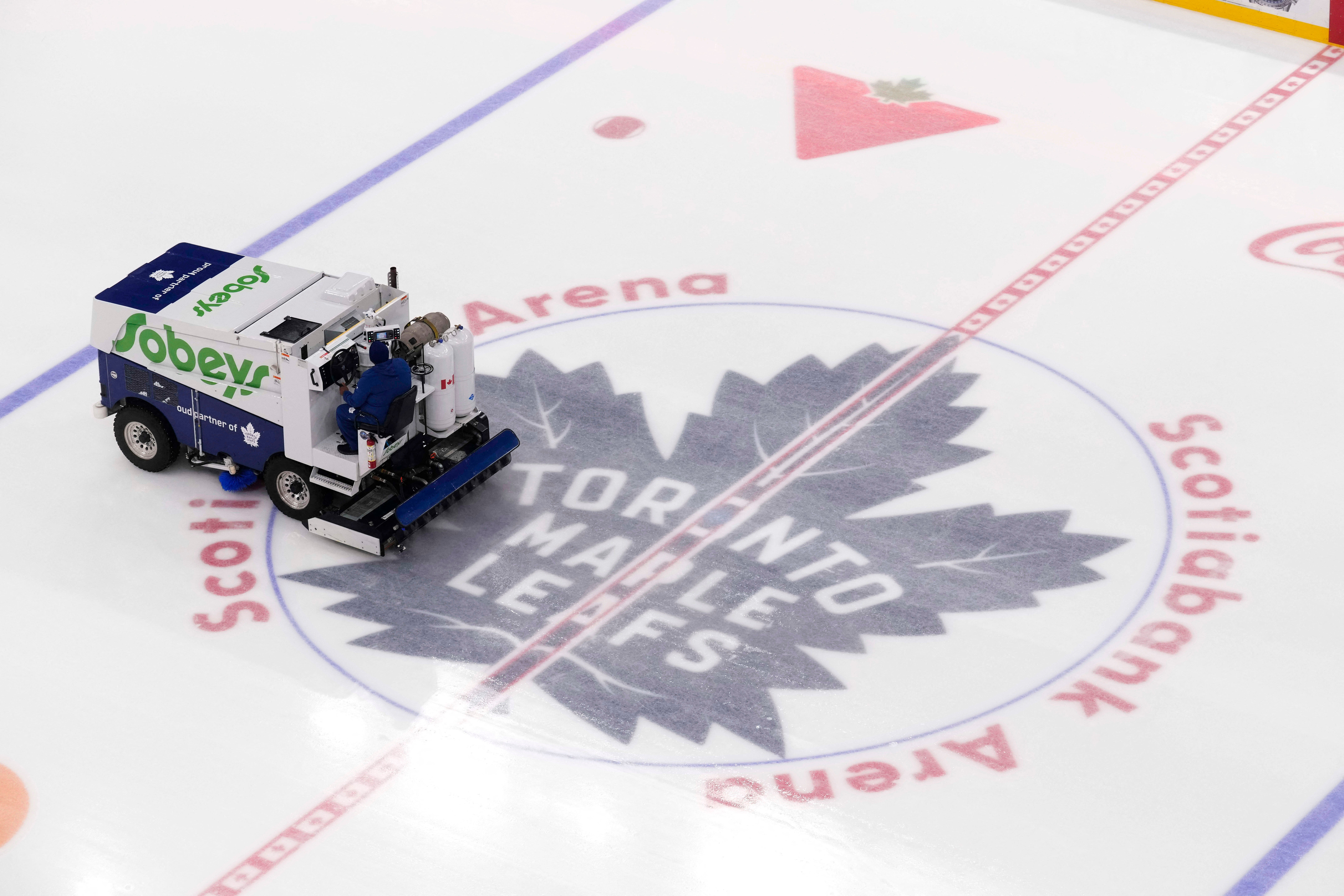 En liten snöröjare på en ishockeyrink med Toronto Maple Leafs logga synlig på isen.
