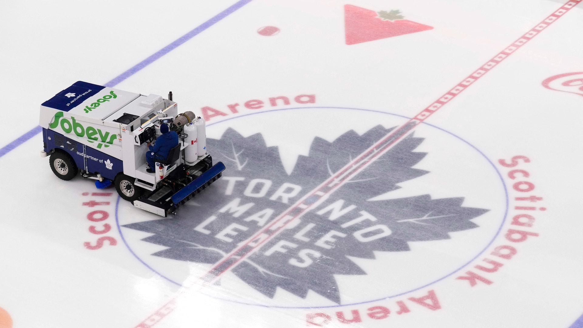 En liten snöröjare på en ishockeyrink med Toronto Maple Leafs logga synlig på isen.