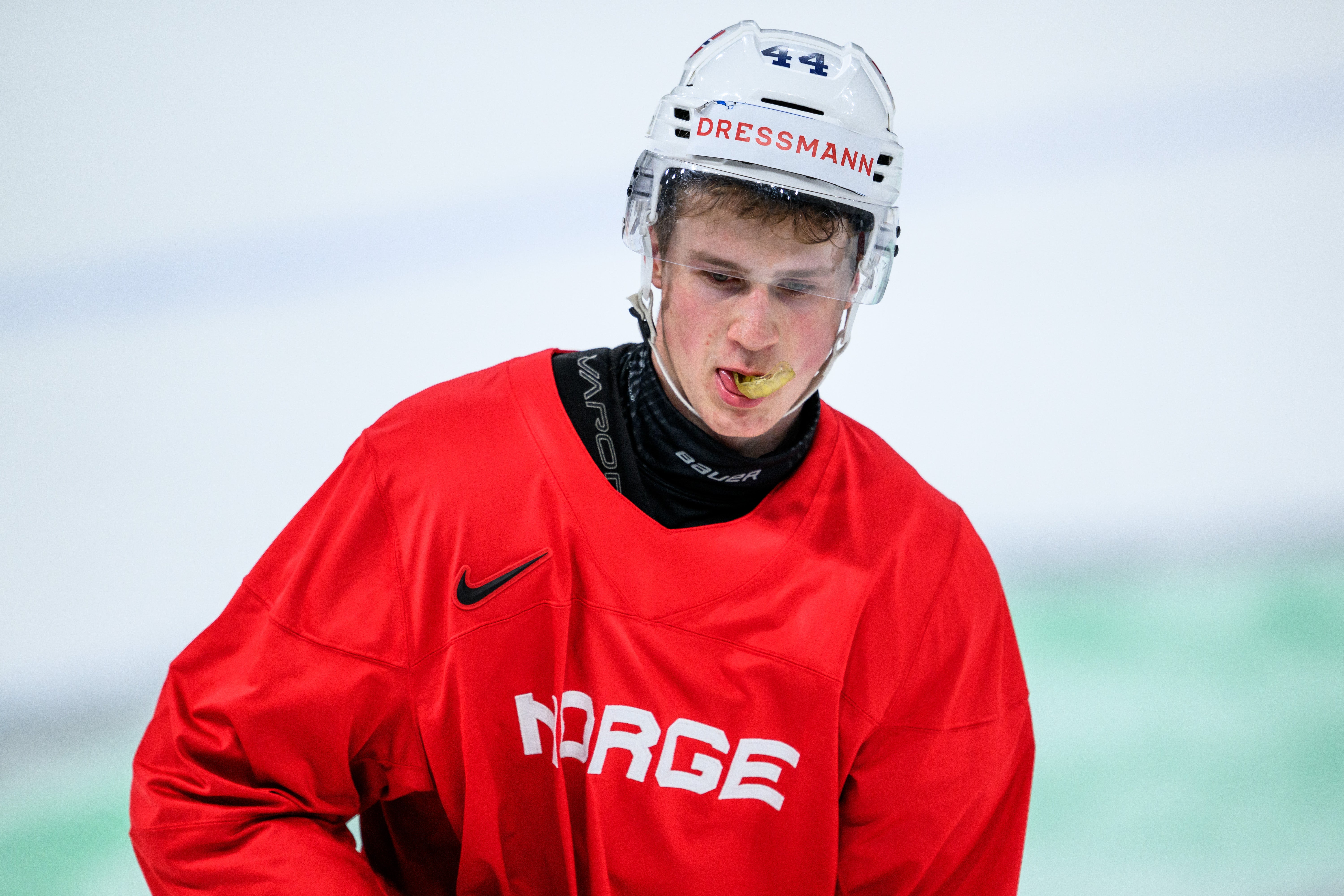 Ung hockeyspelare i röd Norgeströja med vit hjälm under en match. Hockeyspelar i vit tröja med nummer 4 jublar under en match med utstretchad arm.