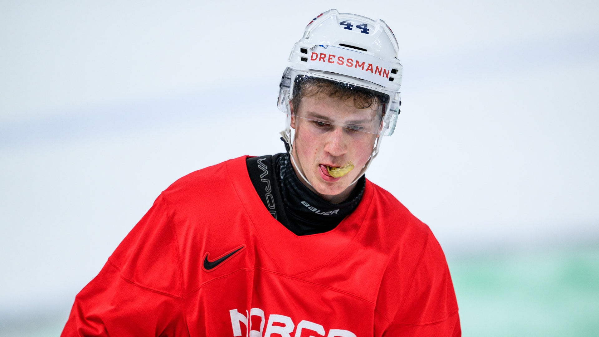 Ung hockeyspelare i röd Norgeströja med vit hjälm under en match. Hockeyspelar i vit tröja med nummer 4 jublar under en match med utstretchad arm.