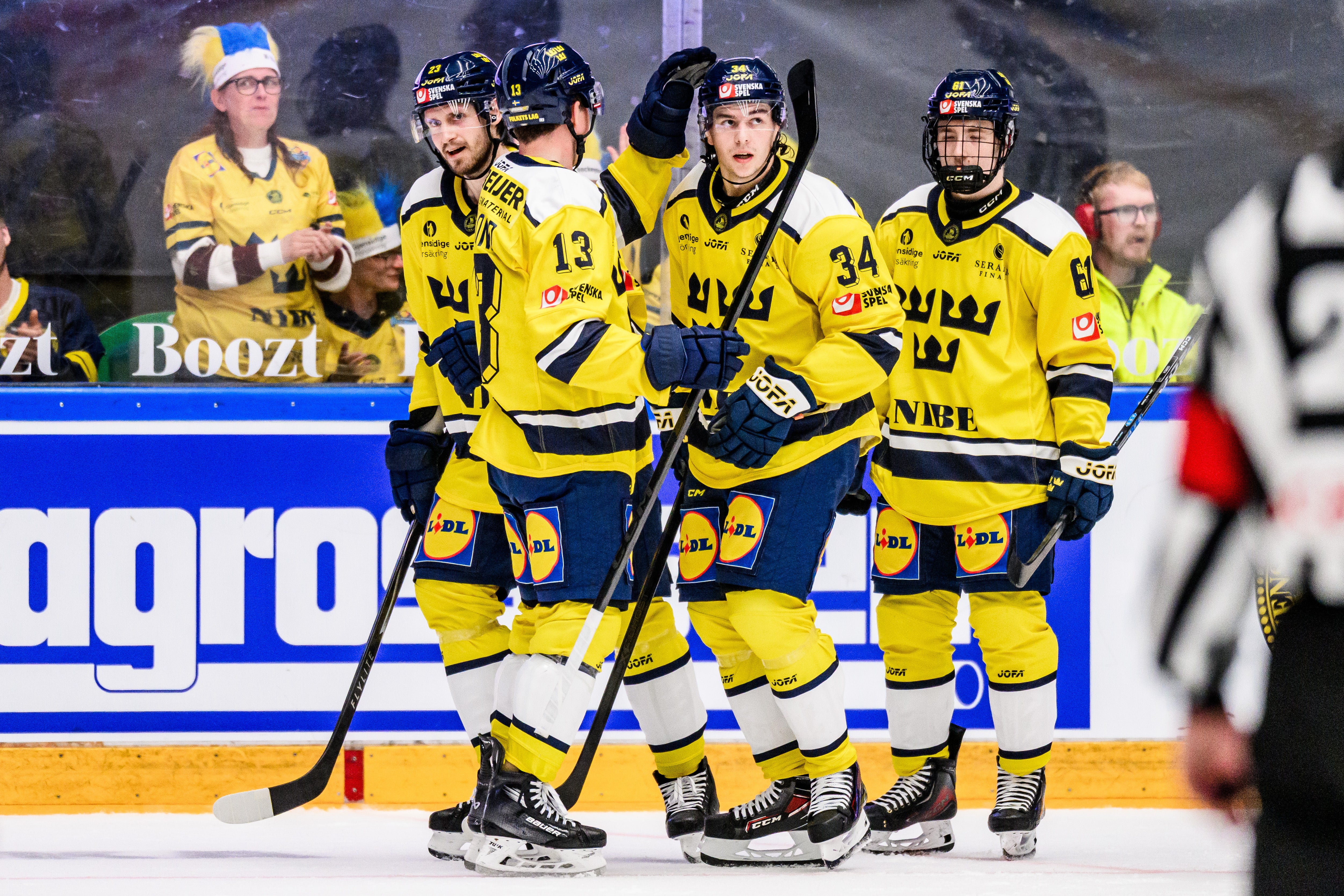 Fyra ishockeyspelare i gula och svarta trikåer står tillsammans på isen under en match.