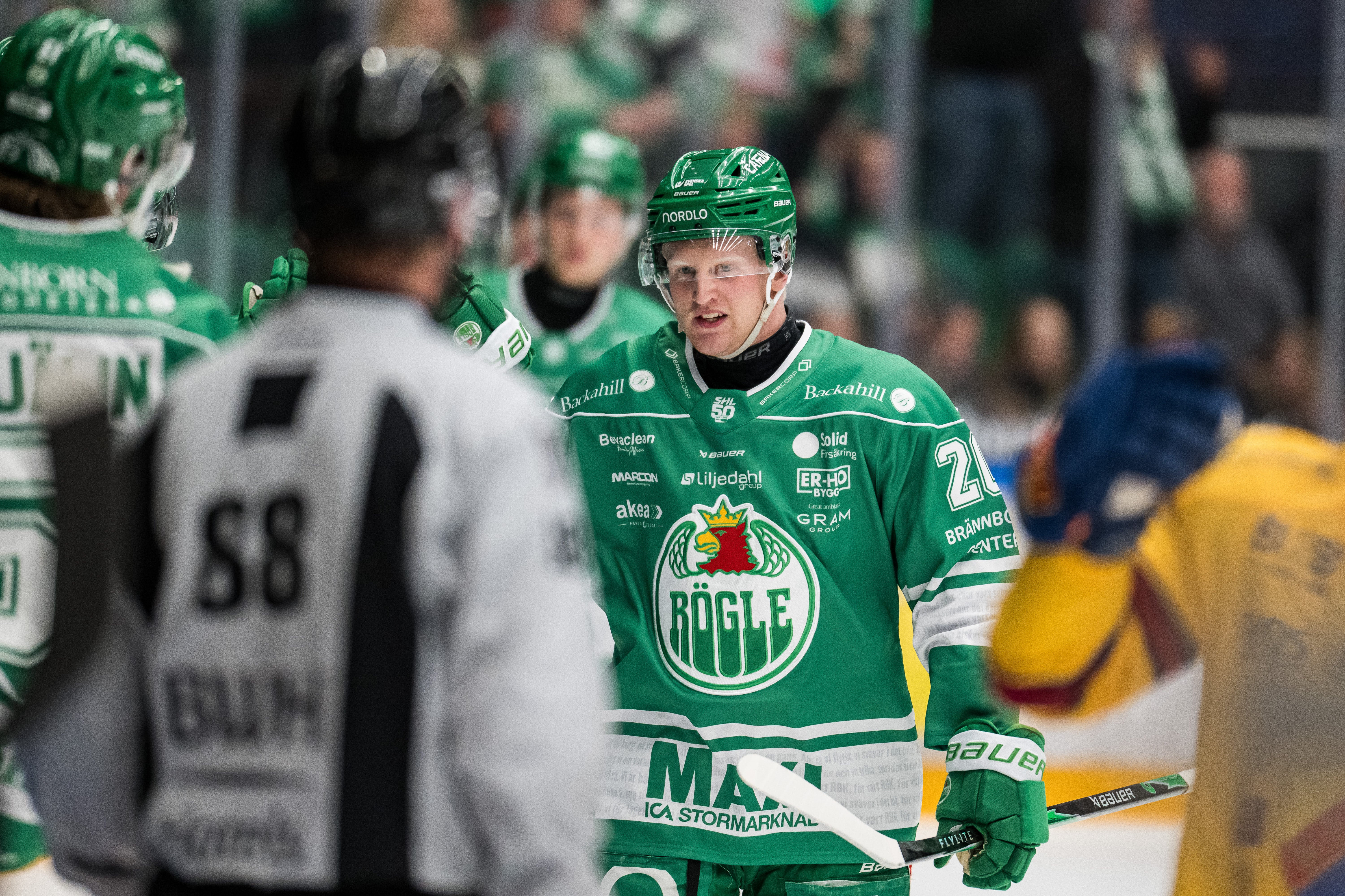 Ishockeyspelare i grön matchdräkt under en ishockeymatch, kommunicerar med lagkamrater på isen.