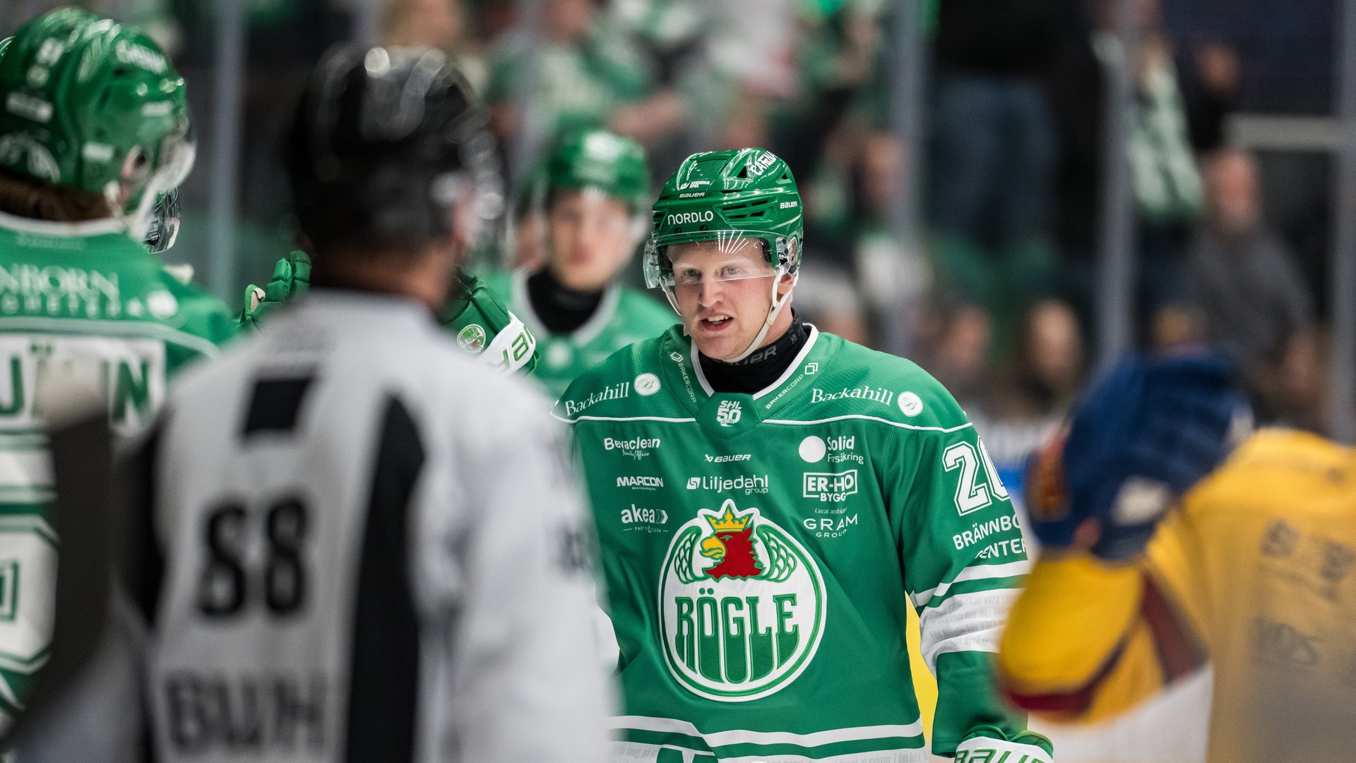 Ishockeyspelare i grön matchdräkt under en ishockeymatch, kommunicerar med lagkamrater på isen.