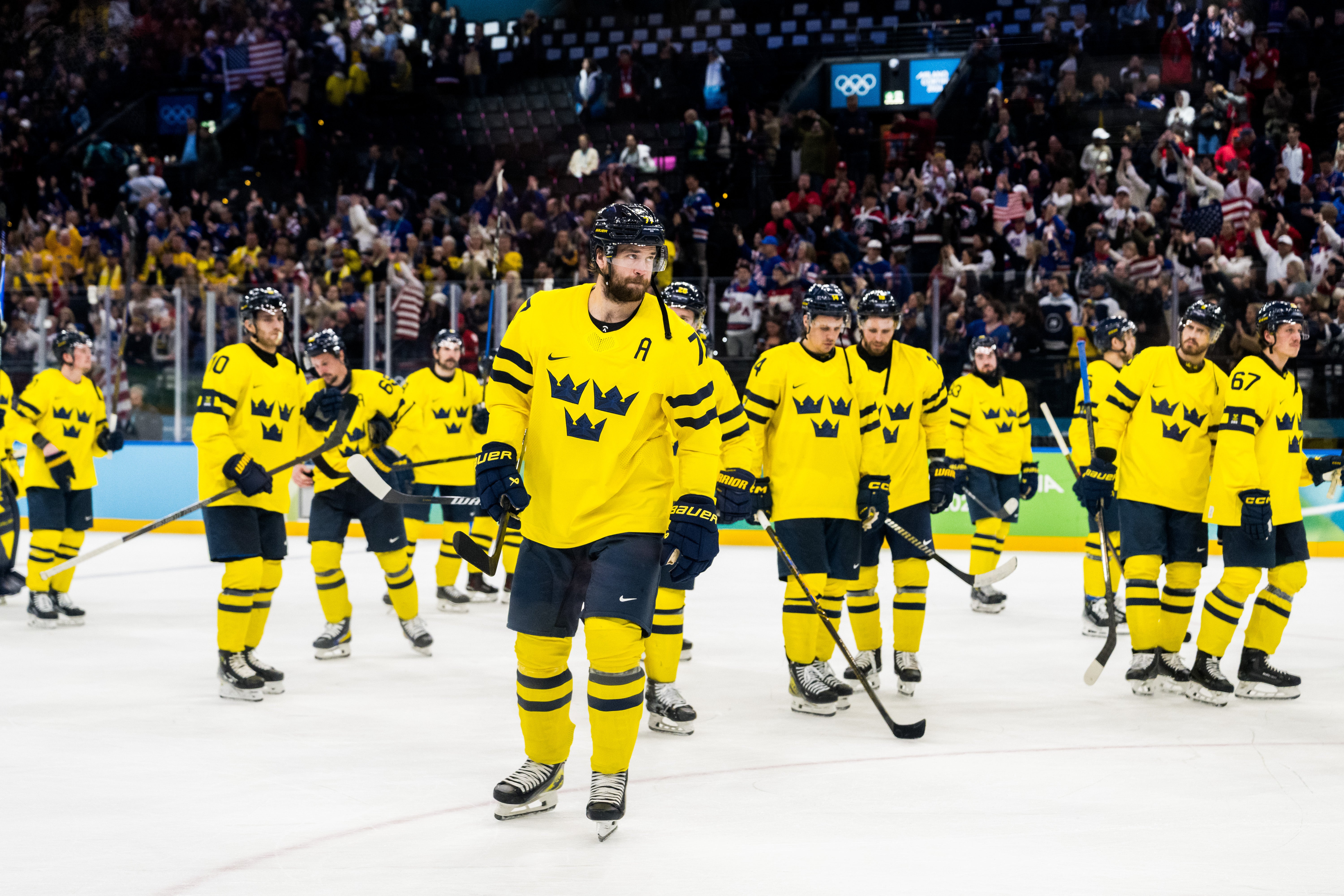 Ishockeylag i gula och svarta trikåer på isen under en match med åskådare i bakgrunden.