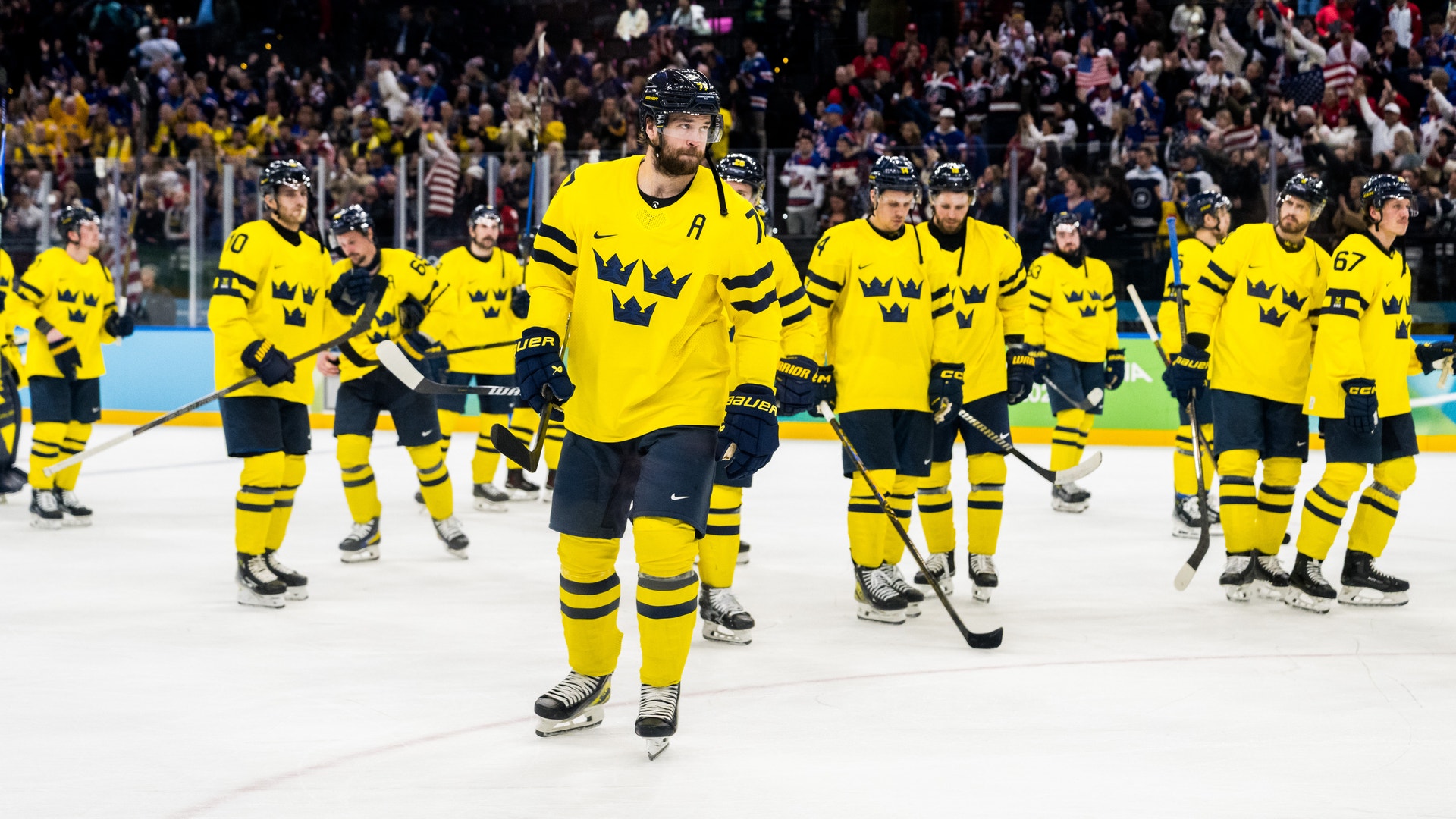 Ishockeylag i gula och svarta trikåer på isen under en match med åskådare i bakgrunden.