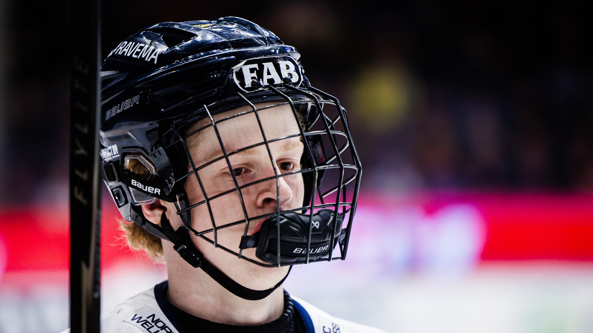 Ishockeyspelare i svart hjälm och vit tröja under en match. Spelaren tittar fokuserat framåt medan han håller i en hockeyklubb.