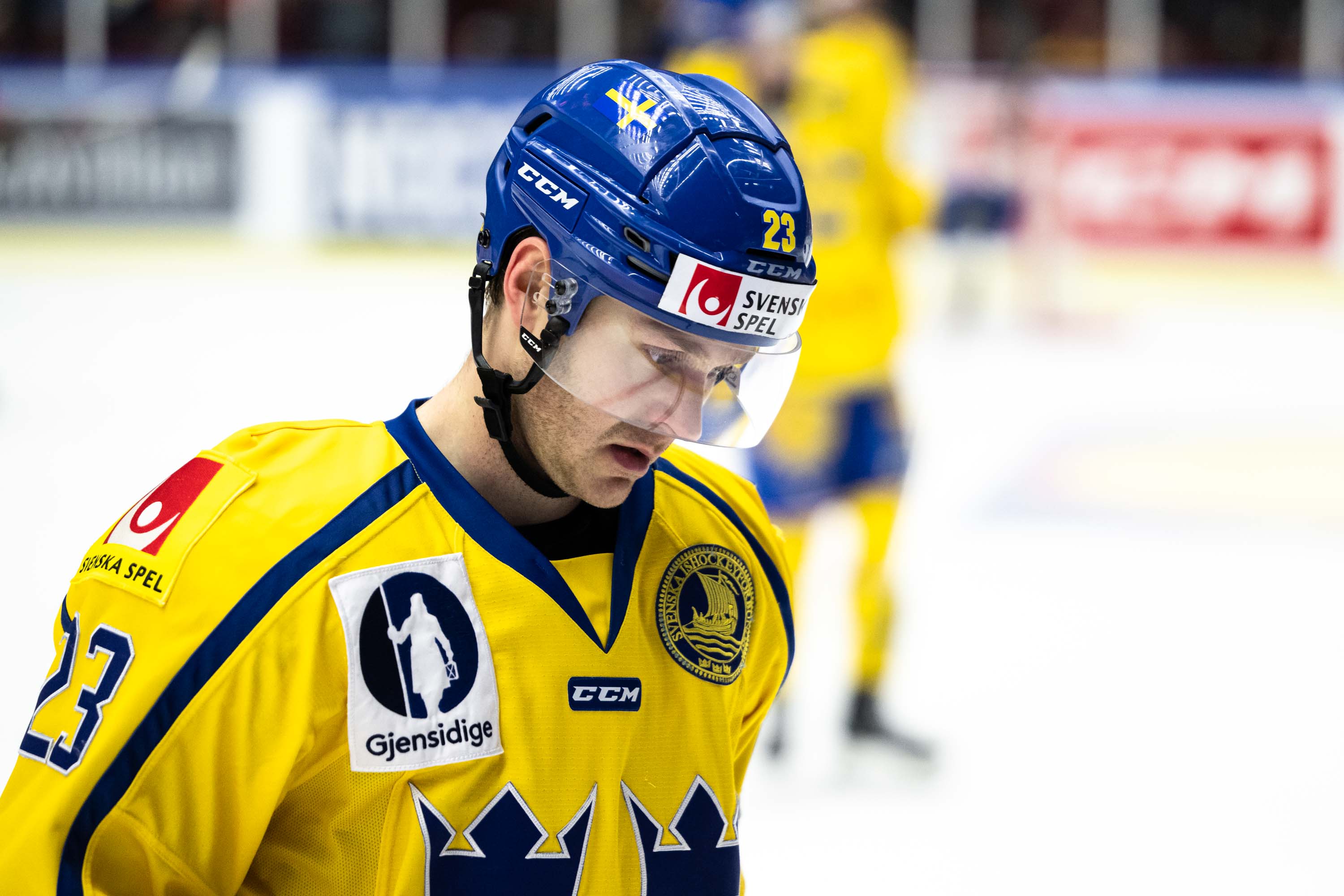 En ishockeyspelare i gul och blå landslagströja med hjälm under en match.