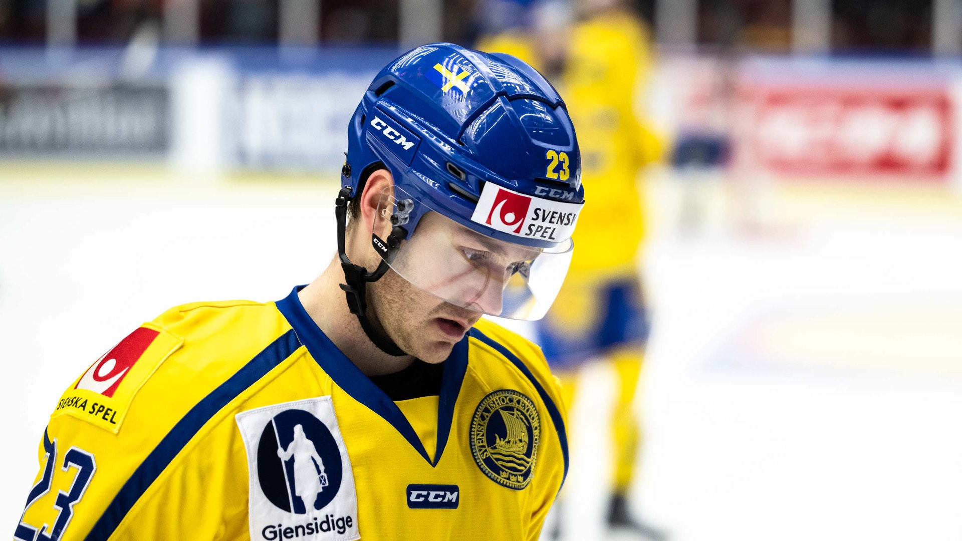 En ishockeyspelare i gul och blå landslagströja med hjälm under en match.
