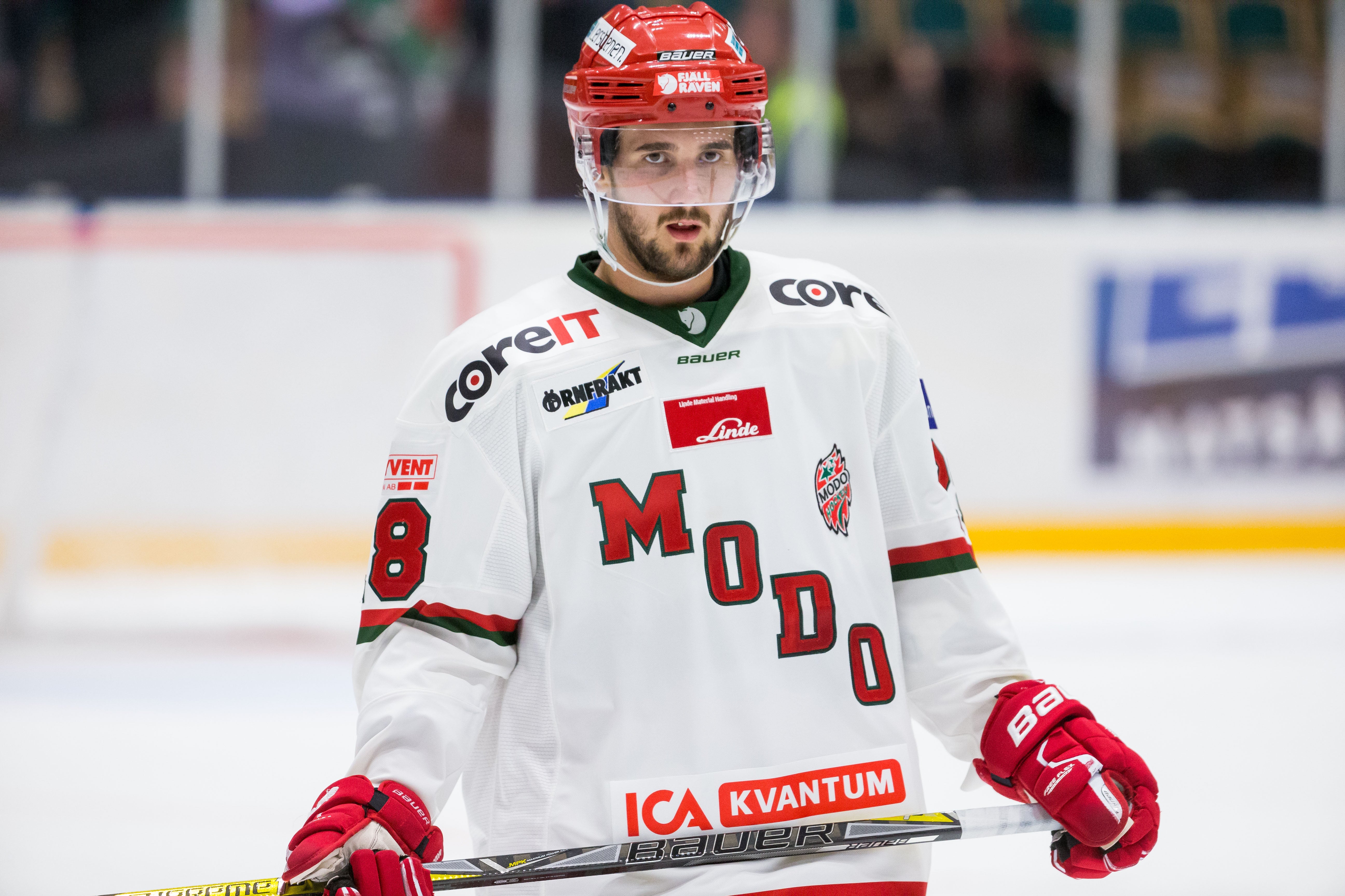 Ishockeyspelare i vit matchdräkt med röd hjälm och röda handskar under en match.