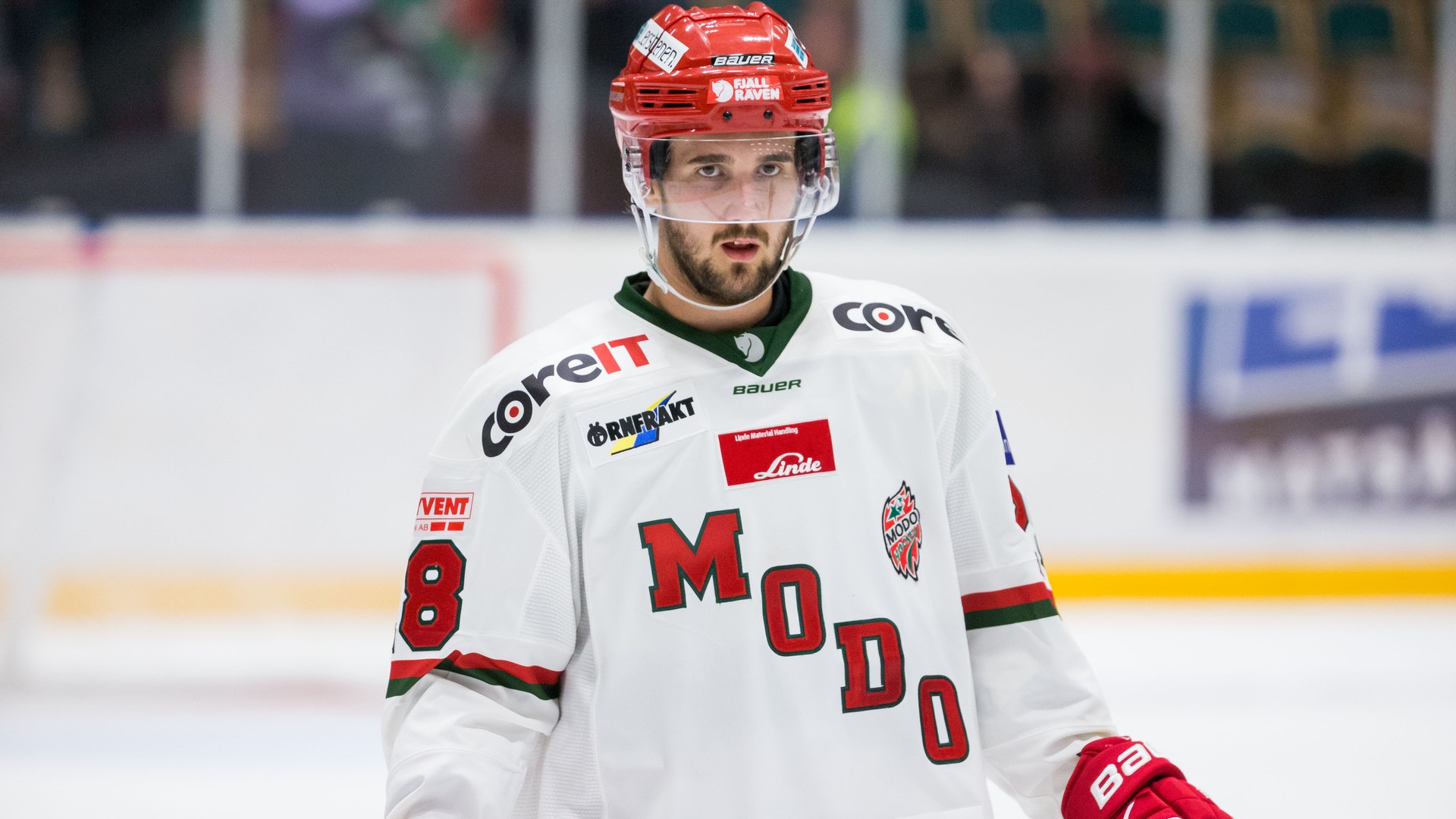 Ishockeyspelare i vit matchdräkt med röd hjälm och röda handskar under en match.