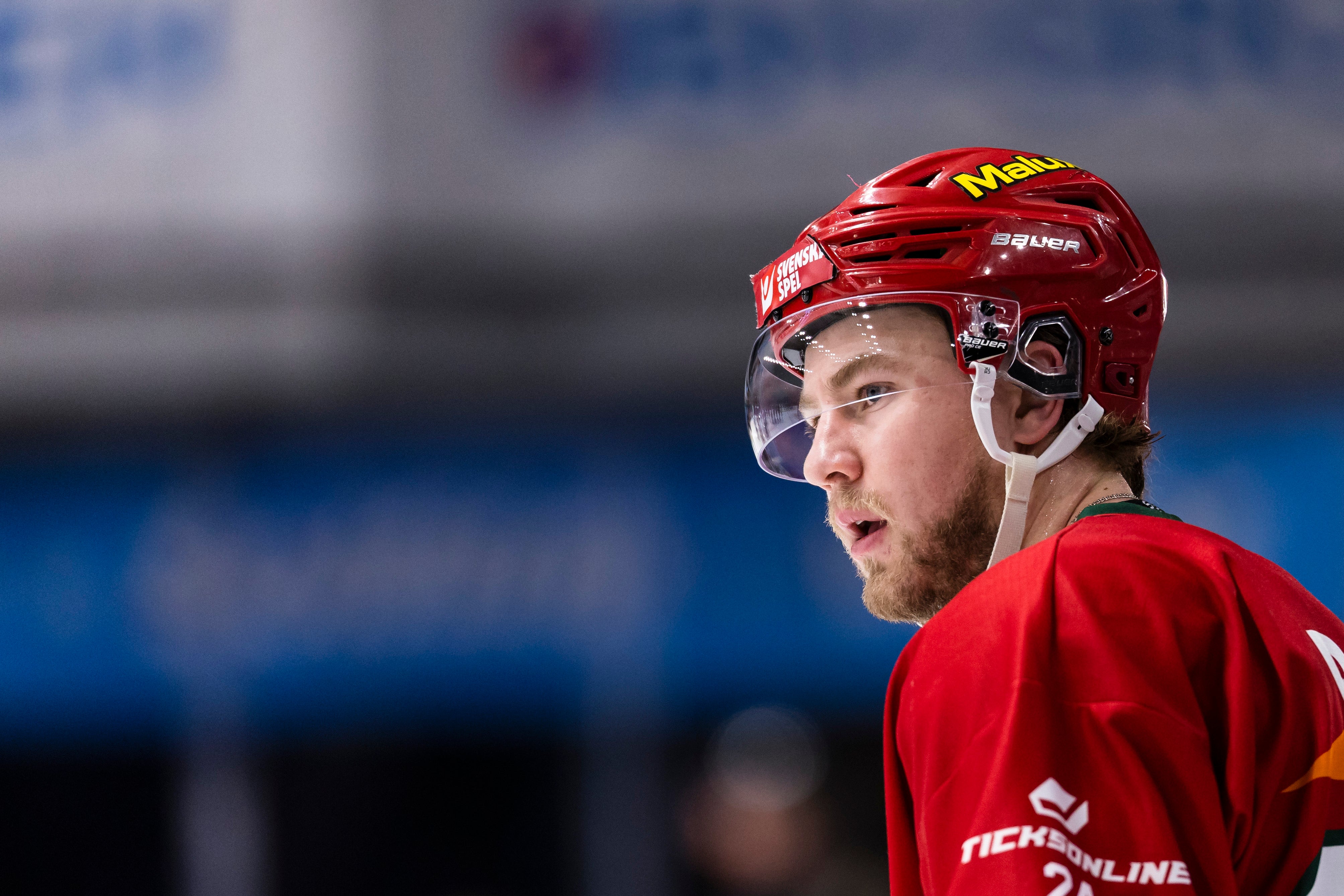En ishockeyspelare i svart och vit tröja med Svenska Spel-loggan på hjälmen, fotograferad under en match.