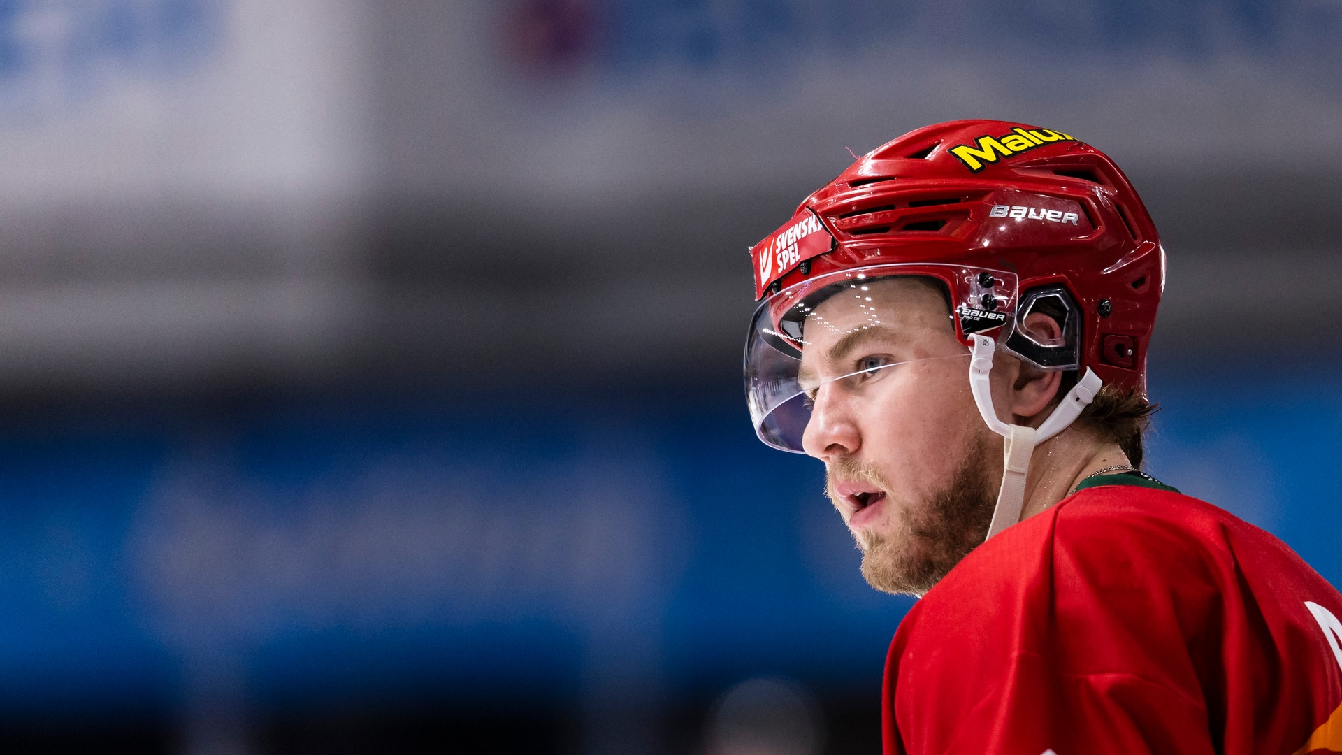 En ishockeyspelare i svart och vit tröja med Svenska Spel-loggan på hjälmen, fotograferad under en match.