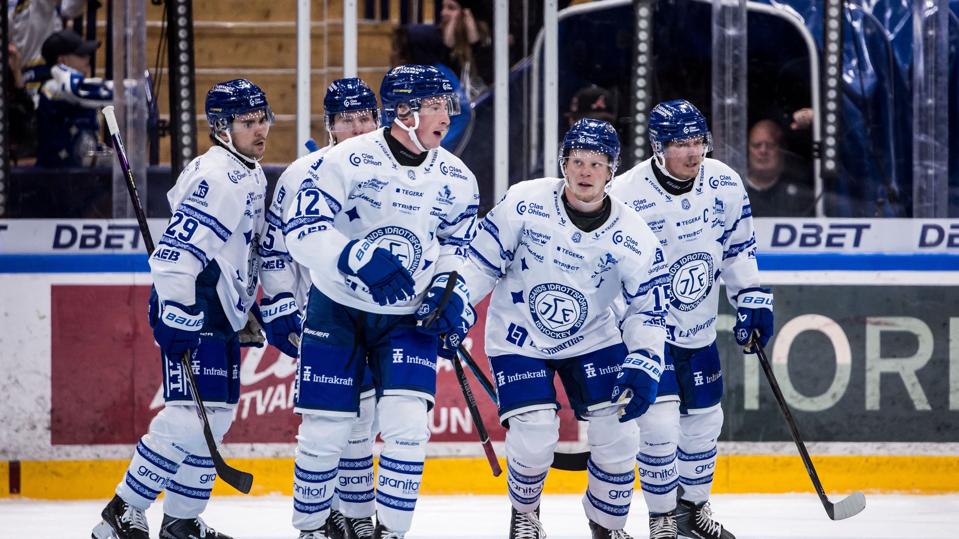 Ishockeyspelare i vita matchtröjor samlas på isen och firar tillsammans under en match.