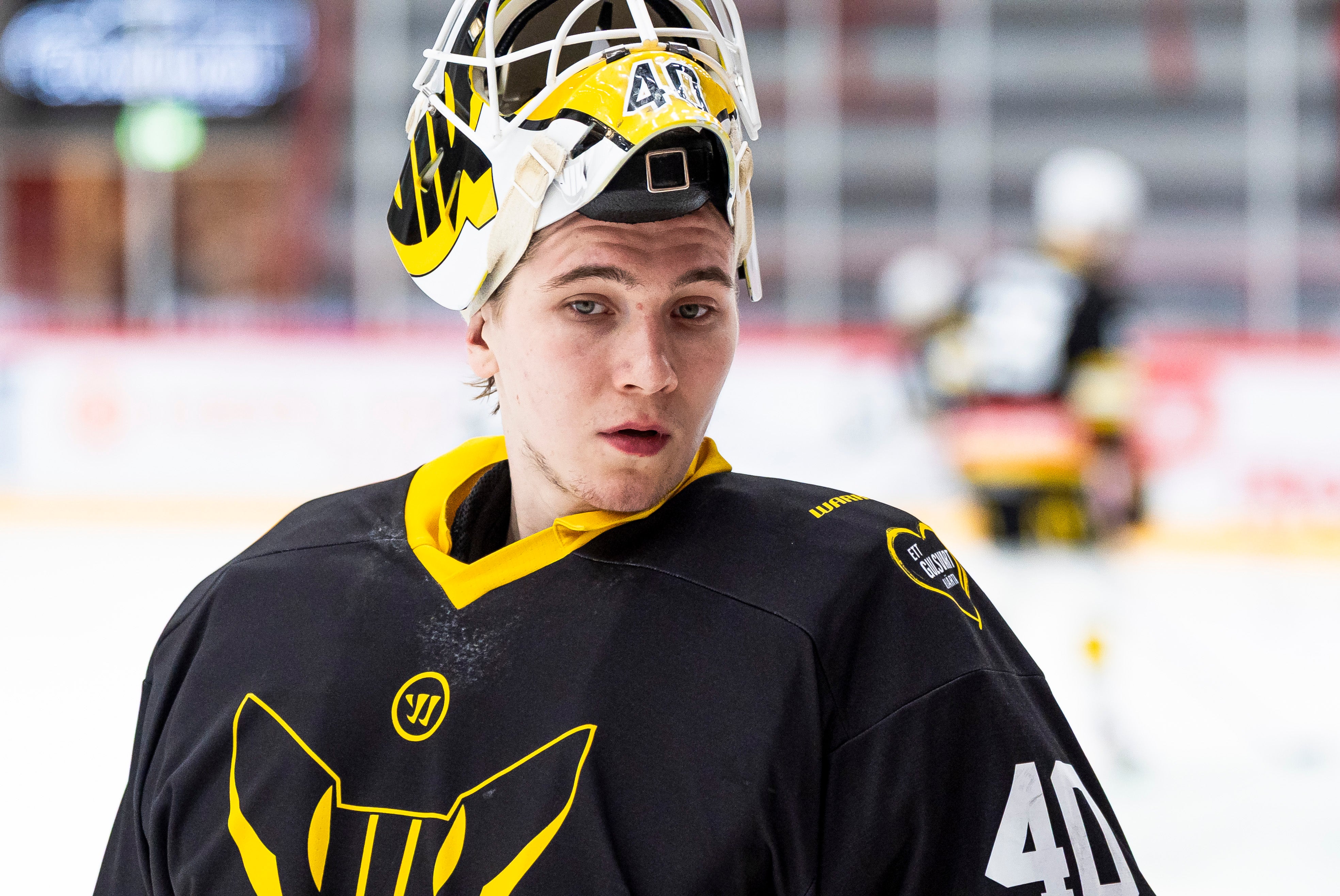 Ishockeyspelare i svart och gul uniform med hjälm på en ishockeybana.