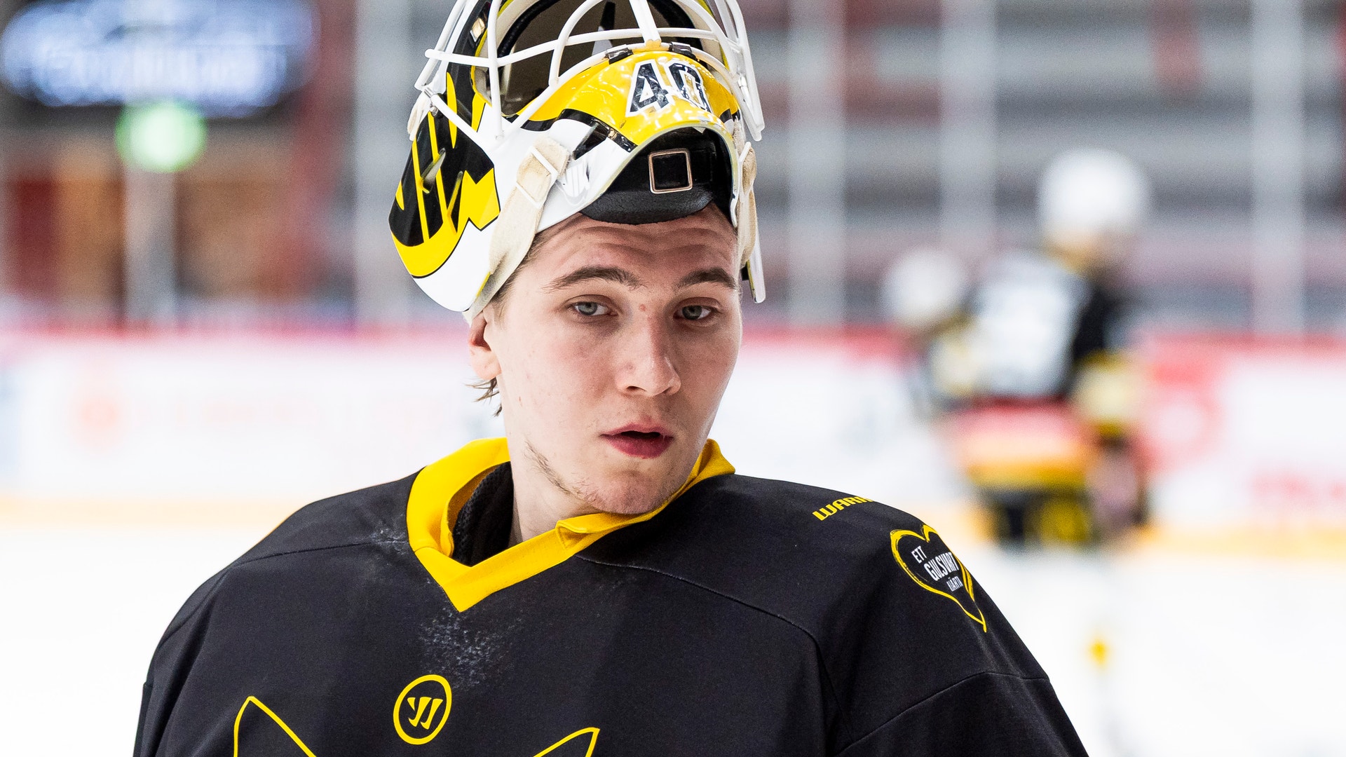 Ishockeyspelare i svart och gul uniform med hjälm på en ishockeybana.
