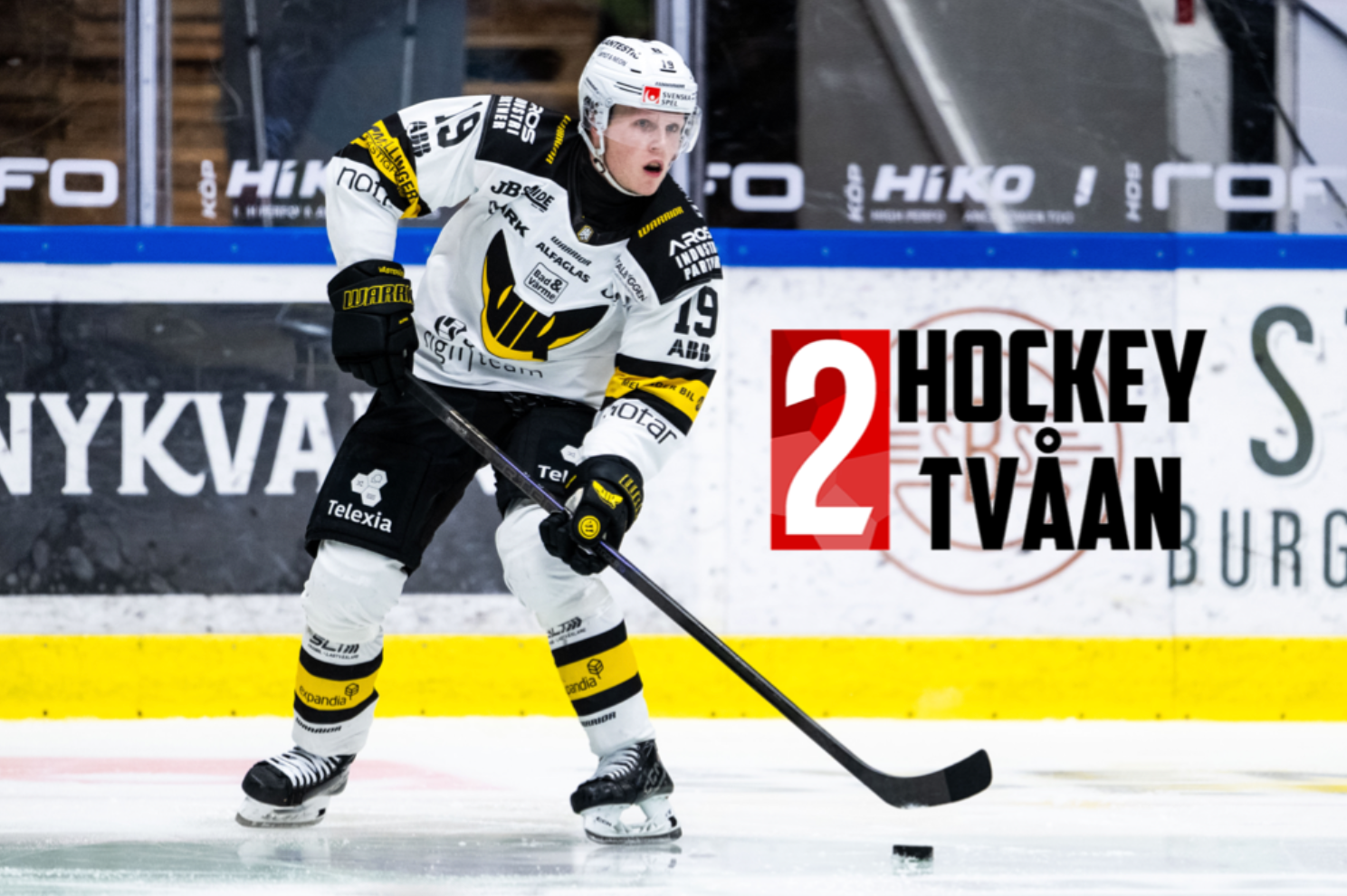 Ishockeyspelare i svart och gul tröja kontrollerar pucken på isen under en match.
