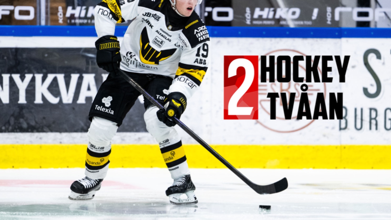 Ishockeyspelare i svart och gul tröja kontrollerar pucken på isen under en match.