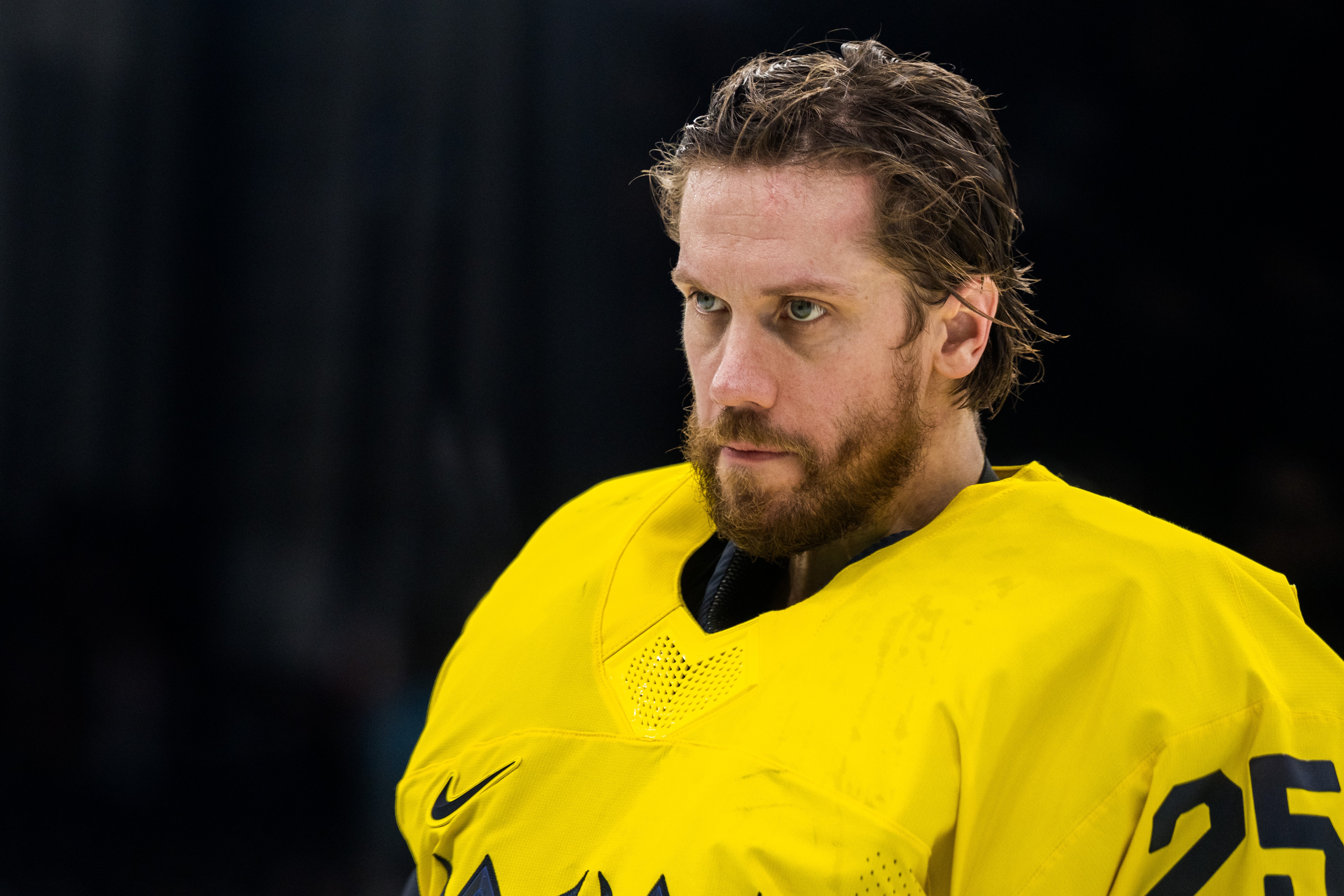 Porträtt av en man i gul ishockeyuniform mot mörk bakgrund.