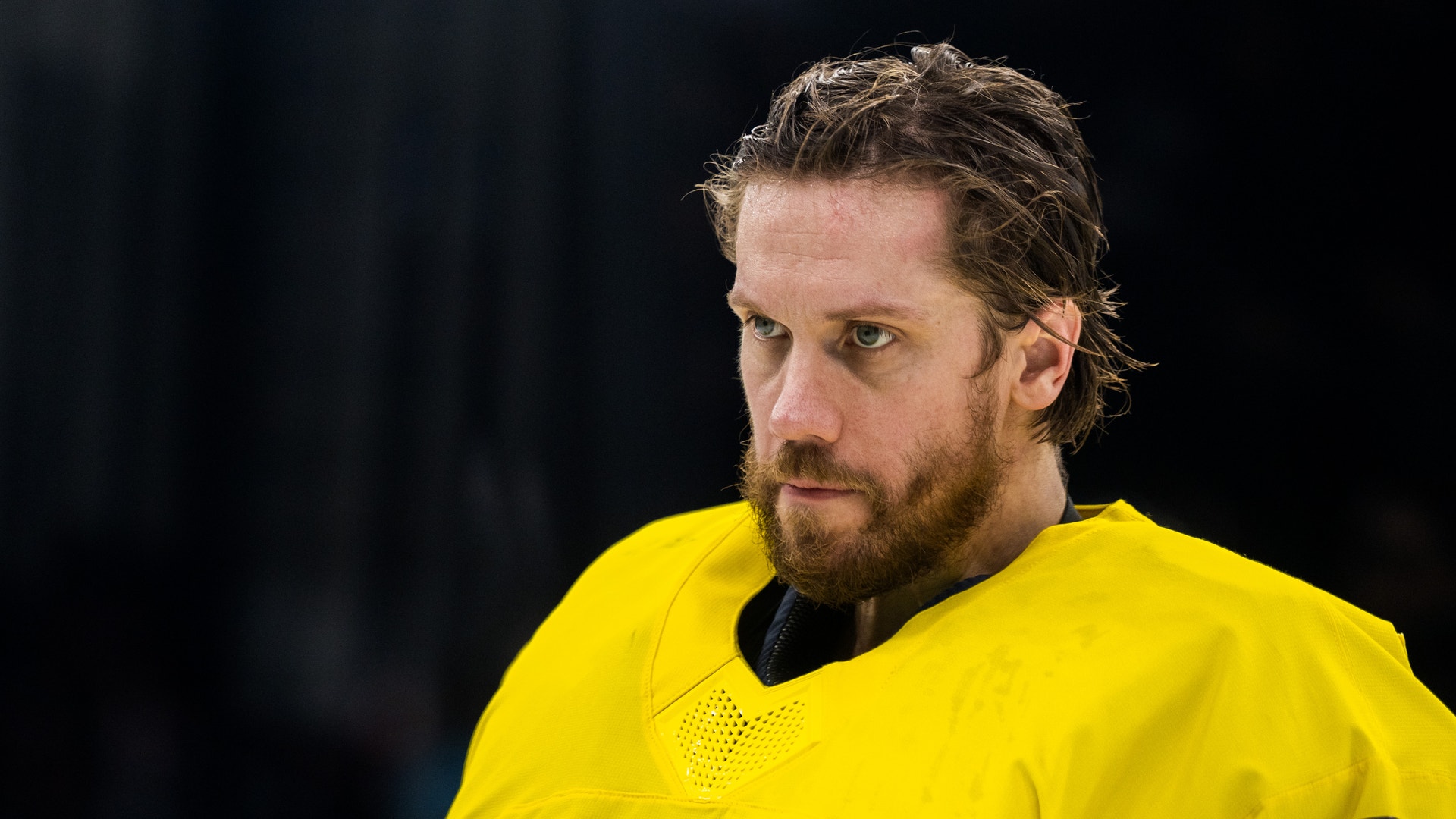Porträtt av en man i gul ishockeyuniform mot mörk bakgrund.