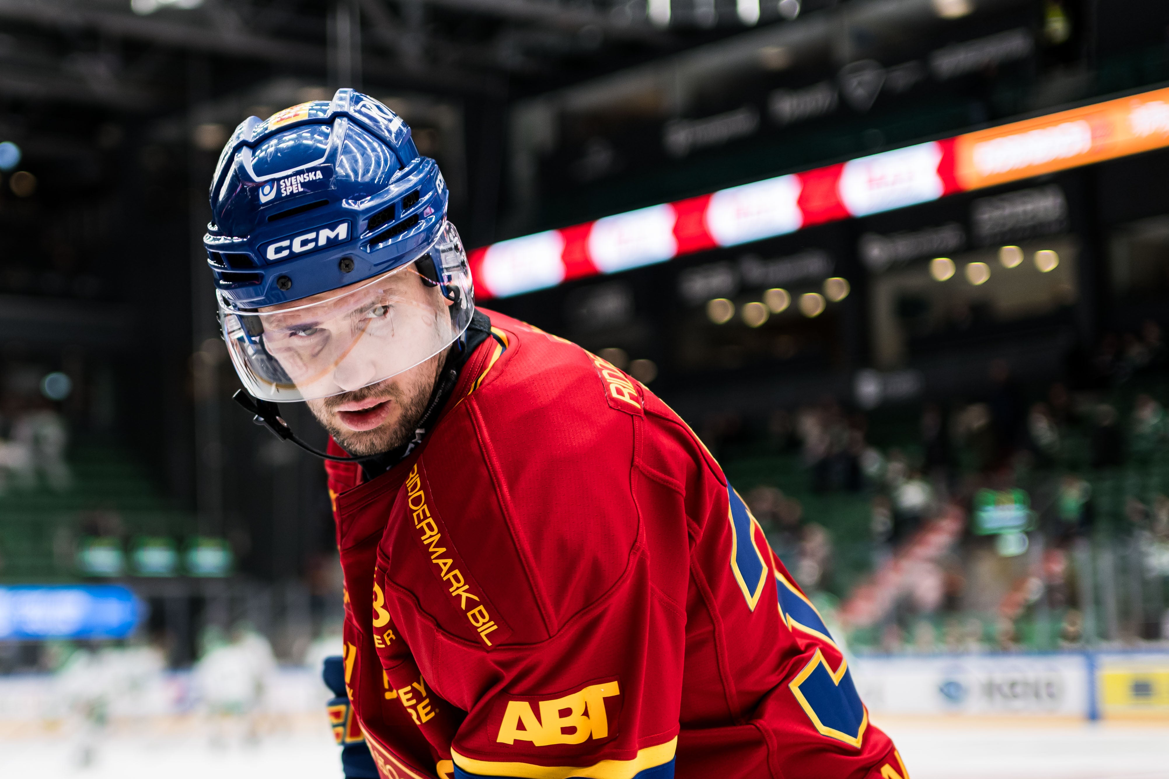 En ishockeyspelare i grön och gul tröja med nummer 32 under en match. Spelaren bär hjälm och ser fokuserad ut. I bakgrunden syns en suddig publik.