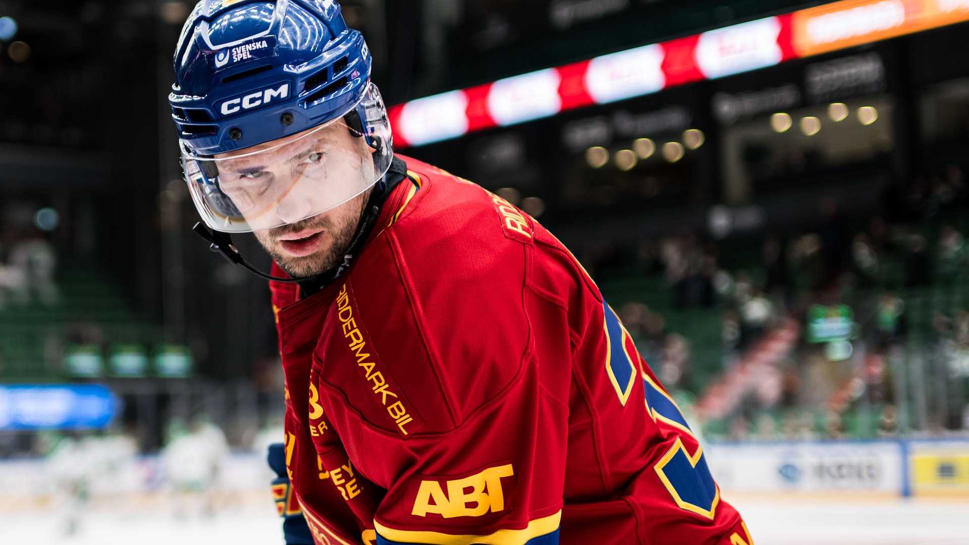 En ishockeyspelare i grön och gul tröja med nummer 32 under en match. Spelaren bär hjälm och ser fokuserad ut. I bakgrunden syns en suddig publik.