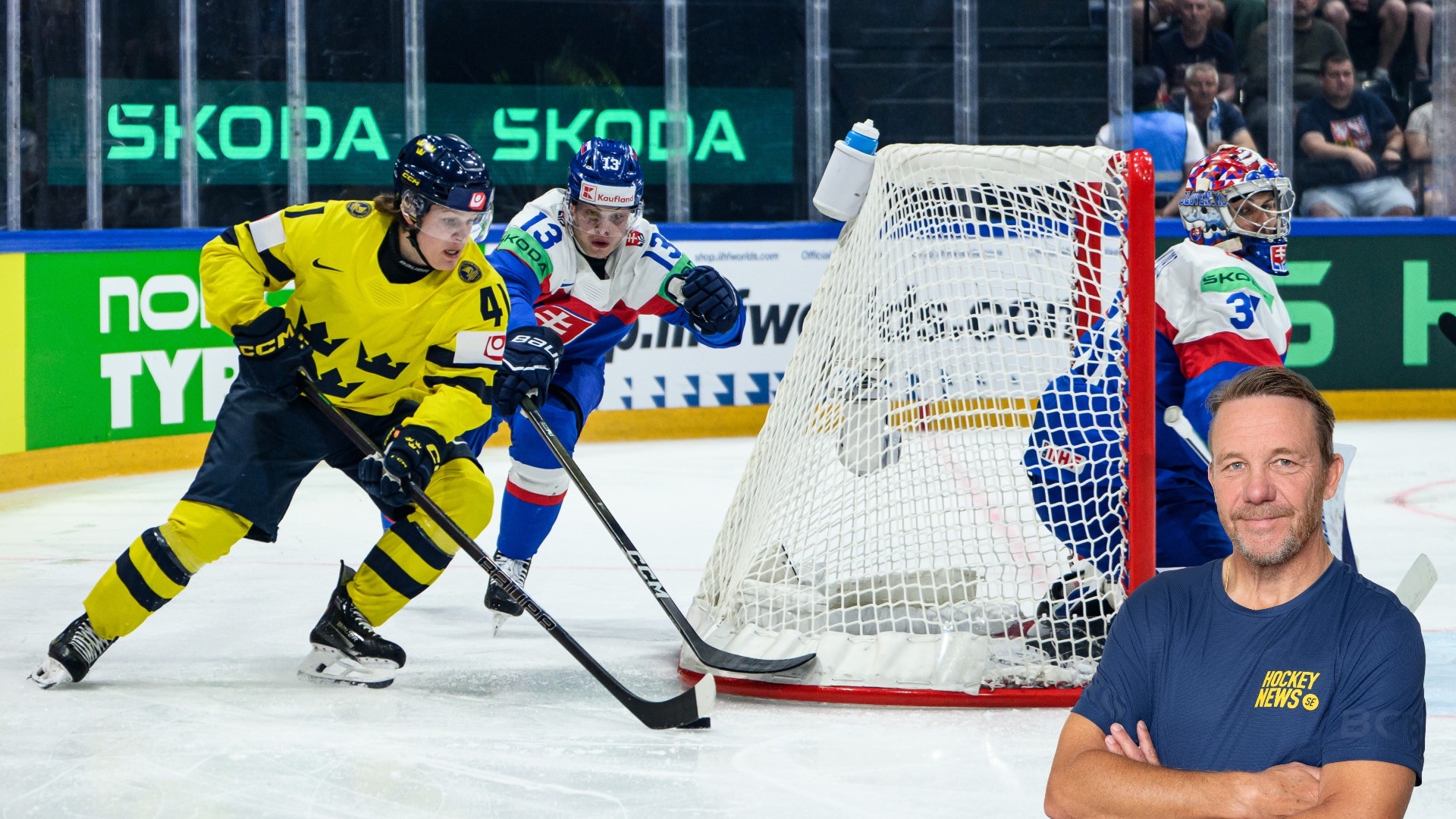 Ishockeyscen där en spelare i gul och svart tröja spelar puck framför målet med en målvakt i röd och blå utrustning. En man i mörkblå tröja visas i förgrunden.