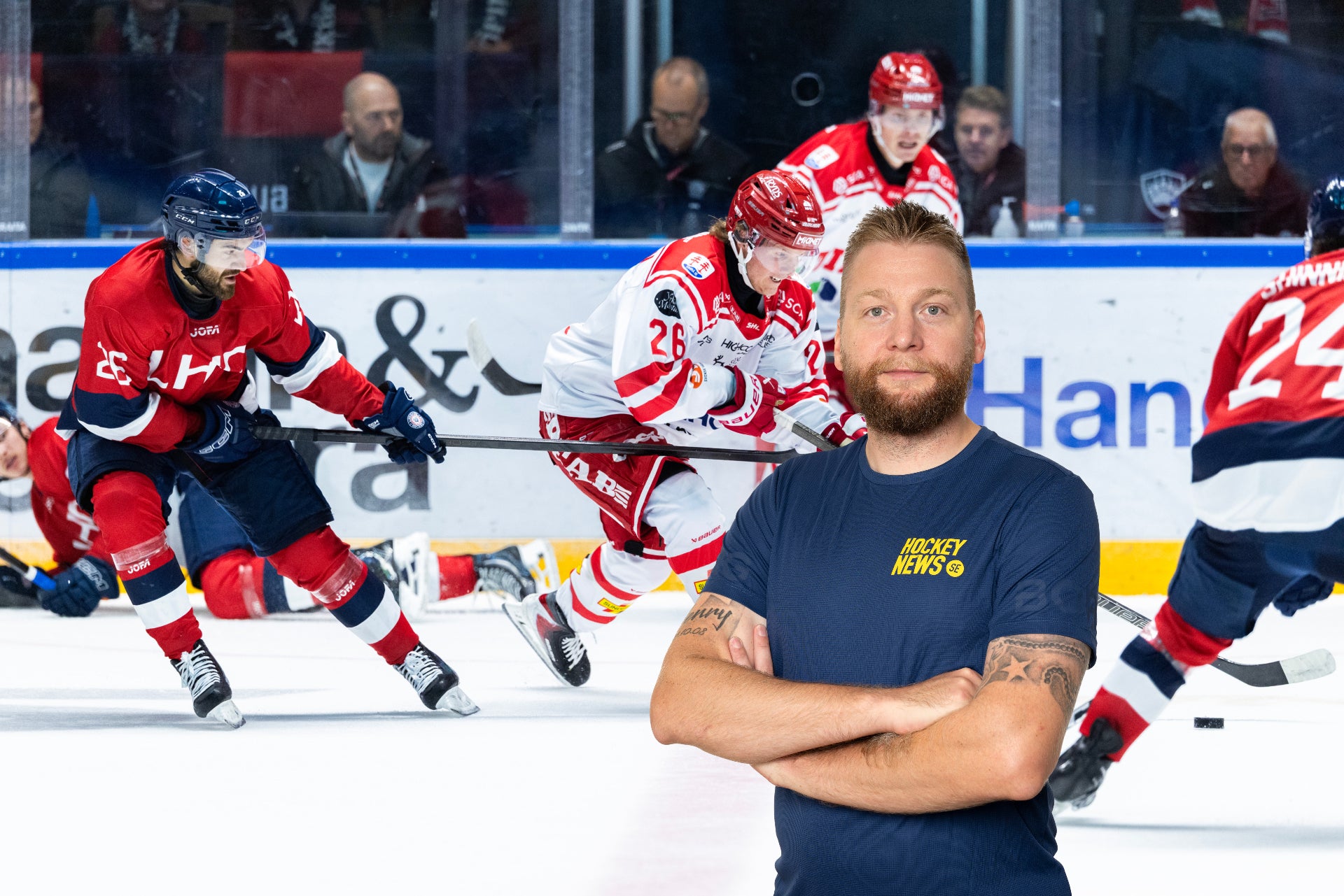 En man med skägg står med armarna korsade framför en ishockeyplan där spelare i röda och blåa matchtröjor spelar match.